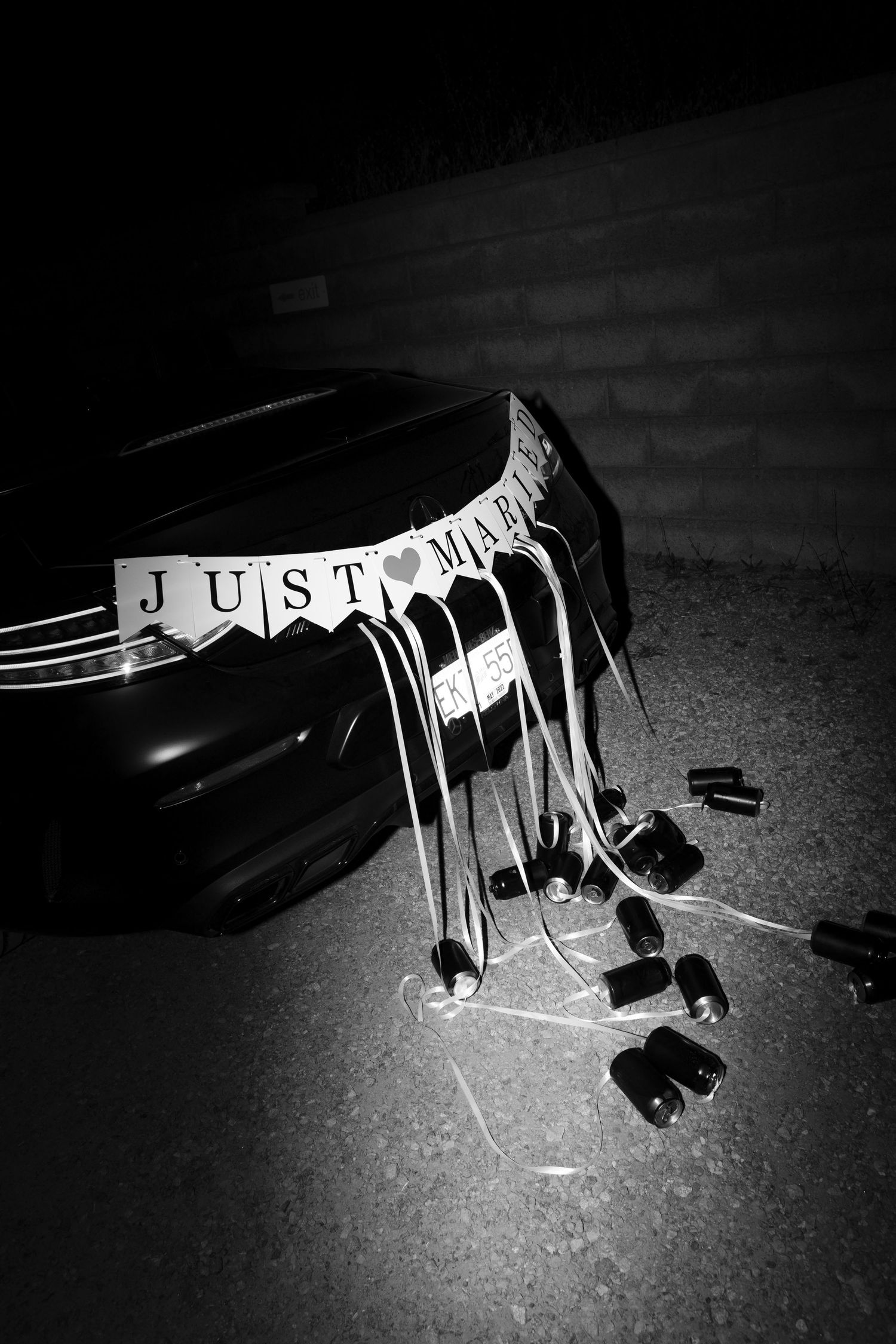 Black and white photo of Just Married banner with tin cans tied to back of wedding getaway car.