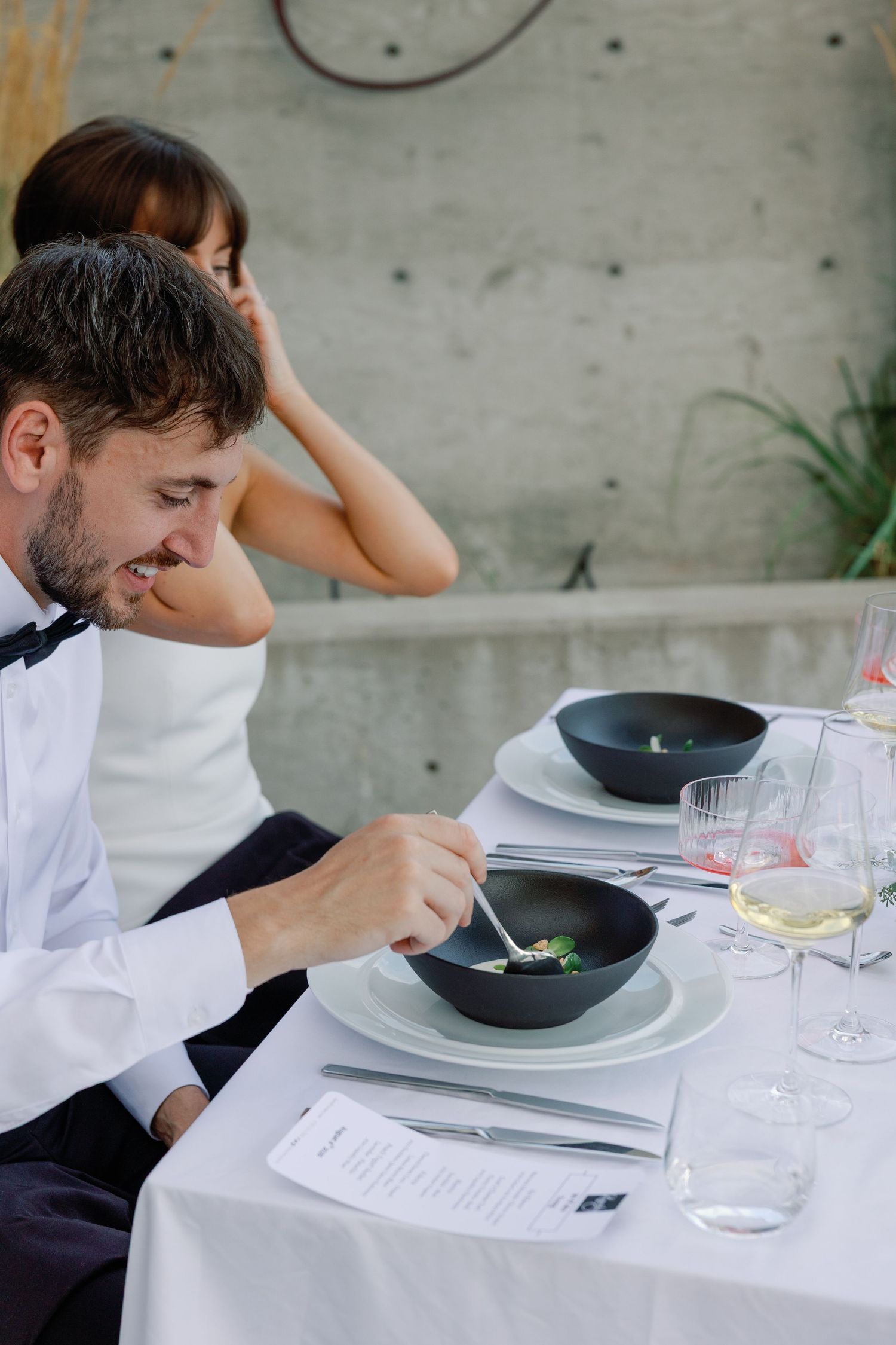 Groom smiles while enjoying elegant plated dish at outdoor winery wedding reception dinner.