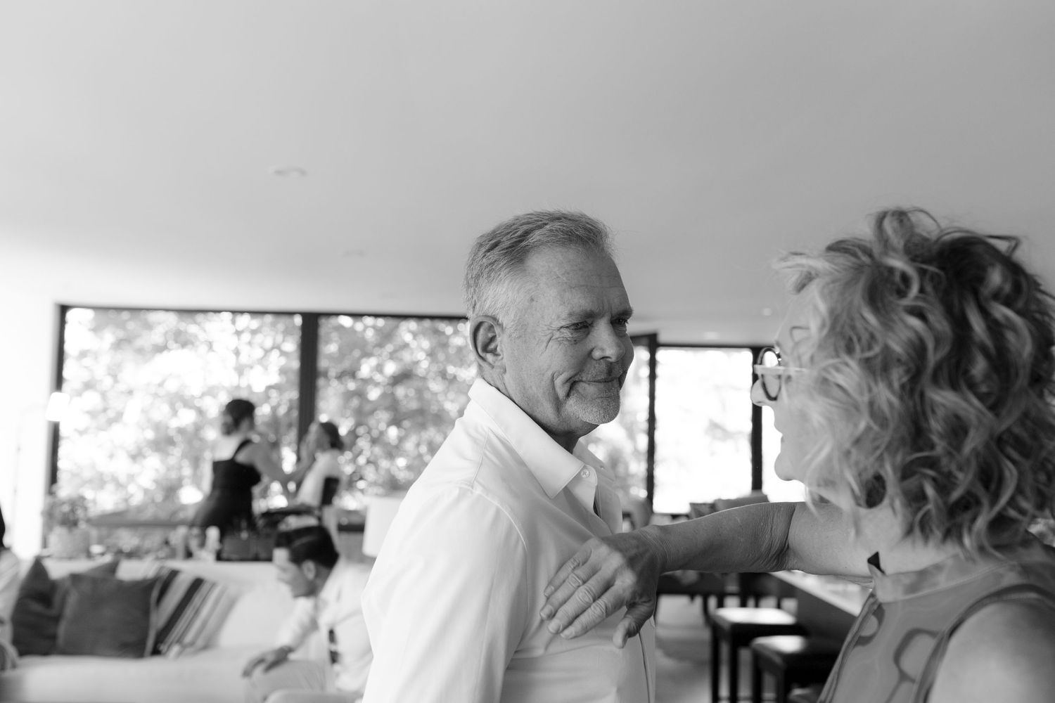 Older couple sharing a warm moment indoors at a wedding reception in black and white photography.
