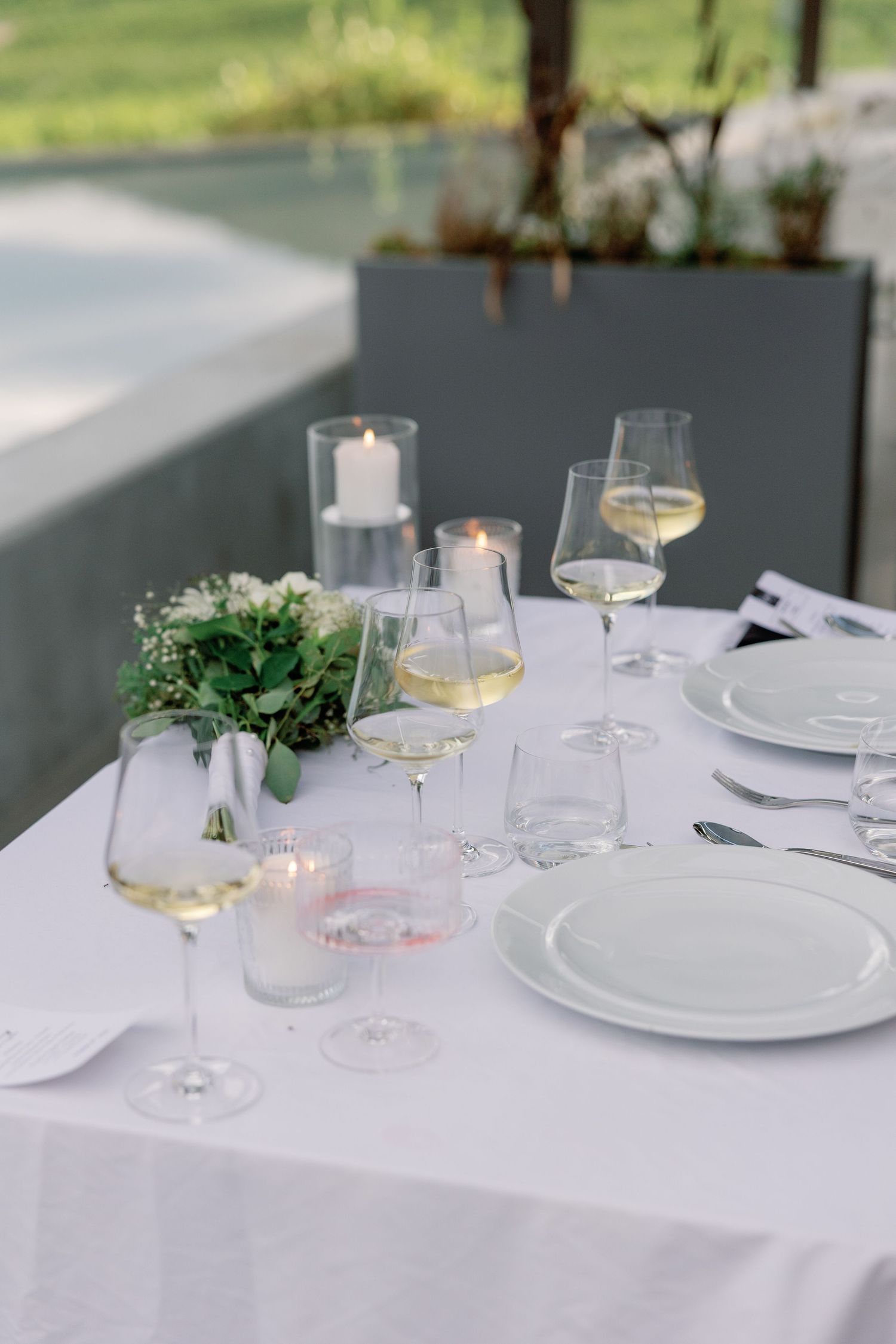 Elegant outdoor wedding reception table with white linen, wine glasses, candles, and floral centerpiece.
