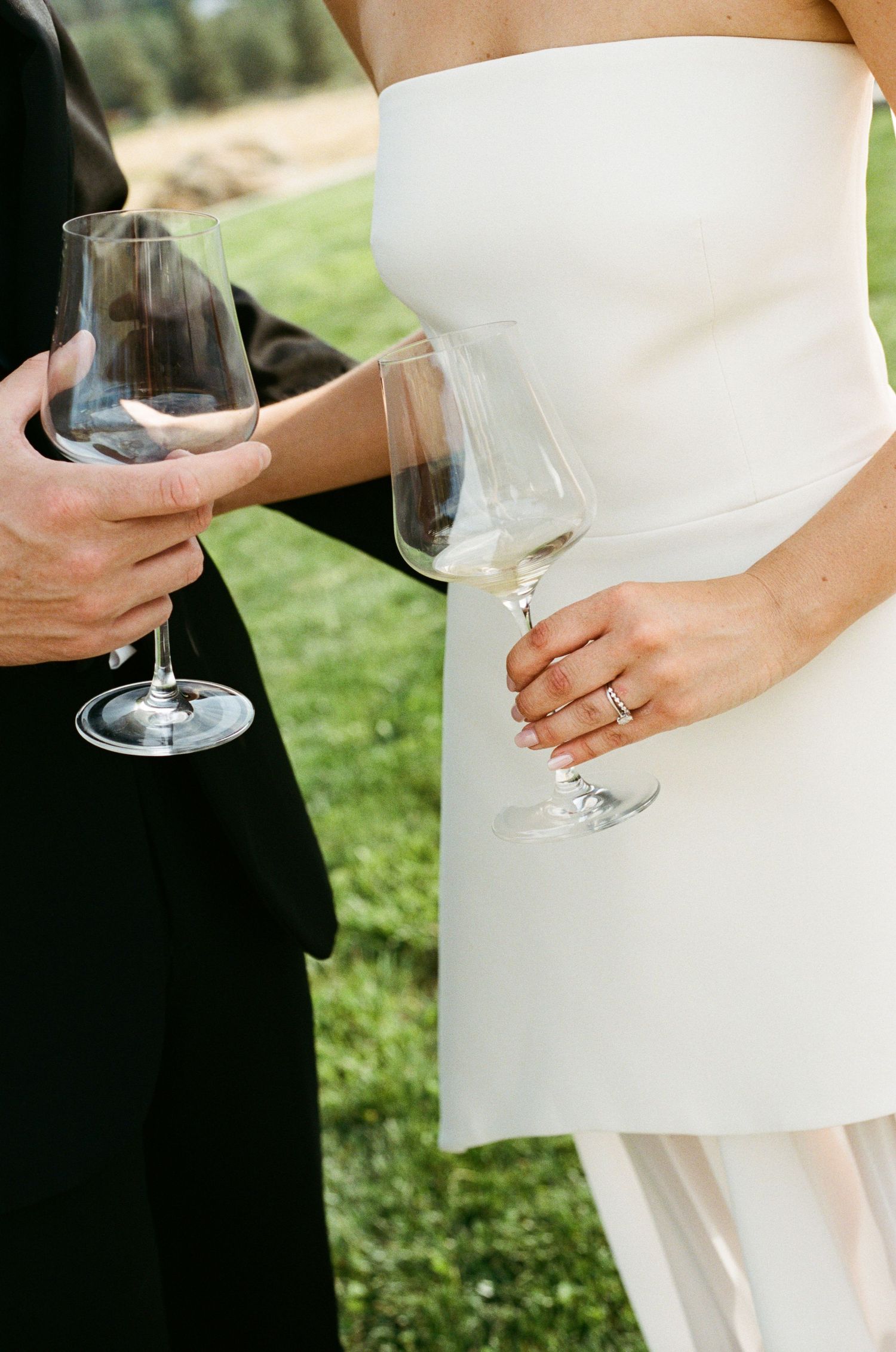 Close-up of bride and groom holding wine glasses, bride wearing diamond wedding ring in white strapless gown.
