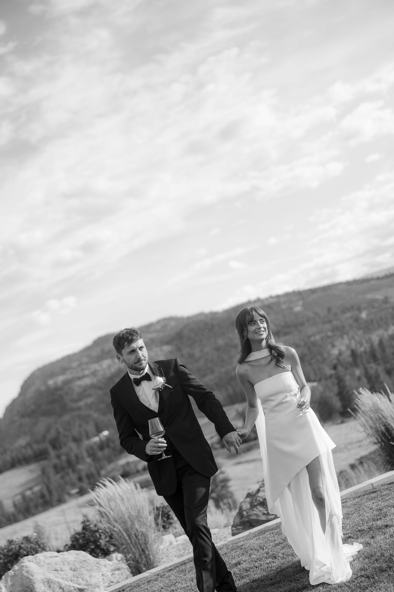 Elegant couple walks hand in hand outdoors with stunning mountain valley views in black and white.