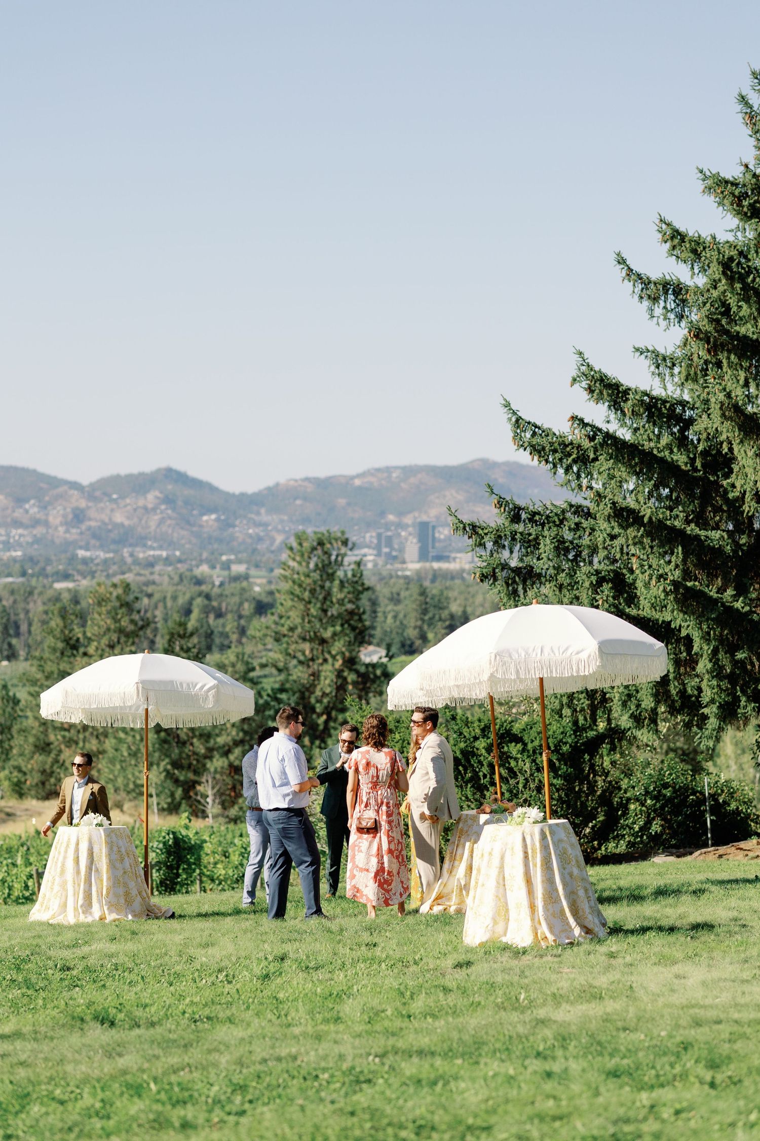 Outdoor wedding cocktail hour with white umbrellas and mountain views in the background.