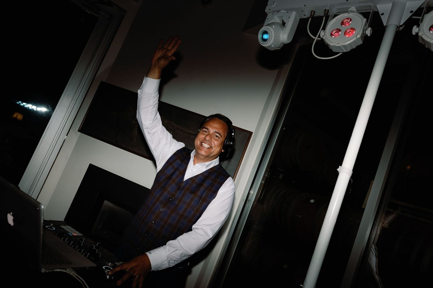 Smiling DJ raises hand while performing at a lively wedding reception.