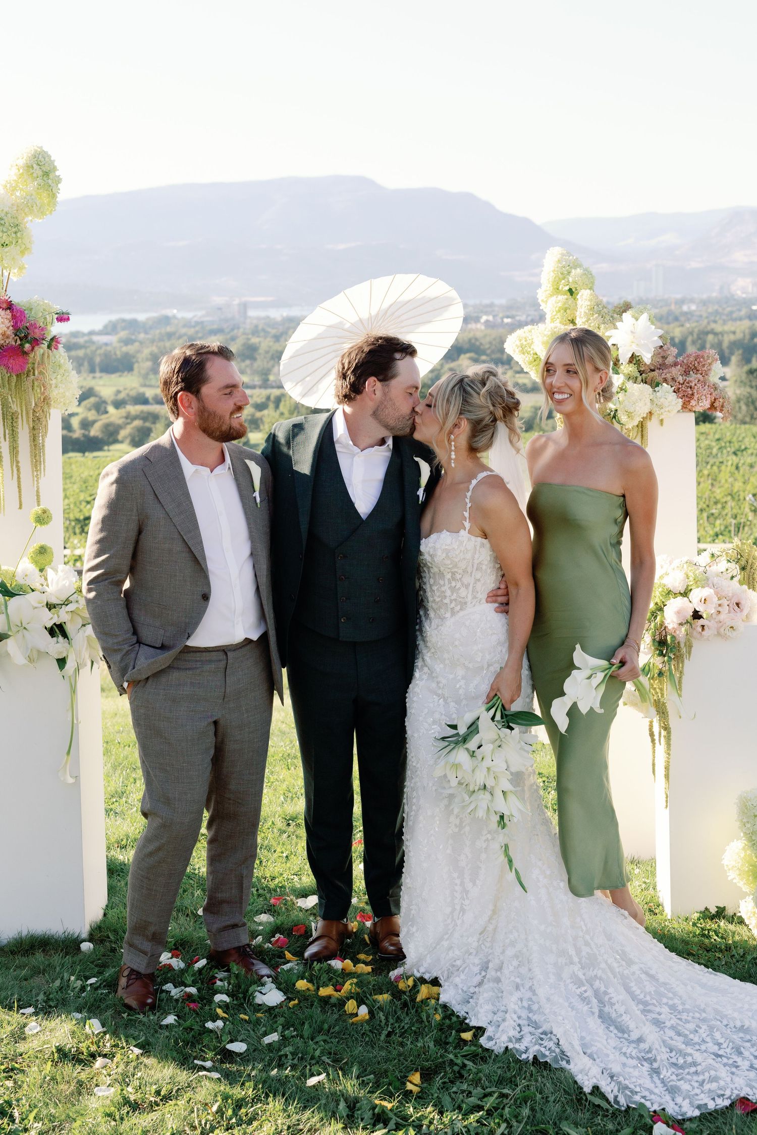 Bride and groom kiss at altar with wedding party beside mountain backdrop.