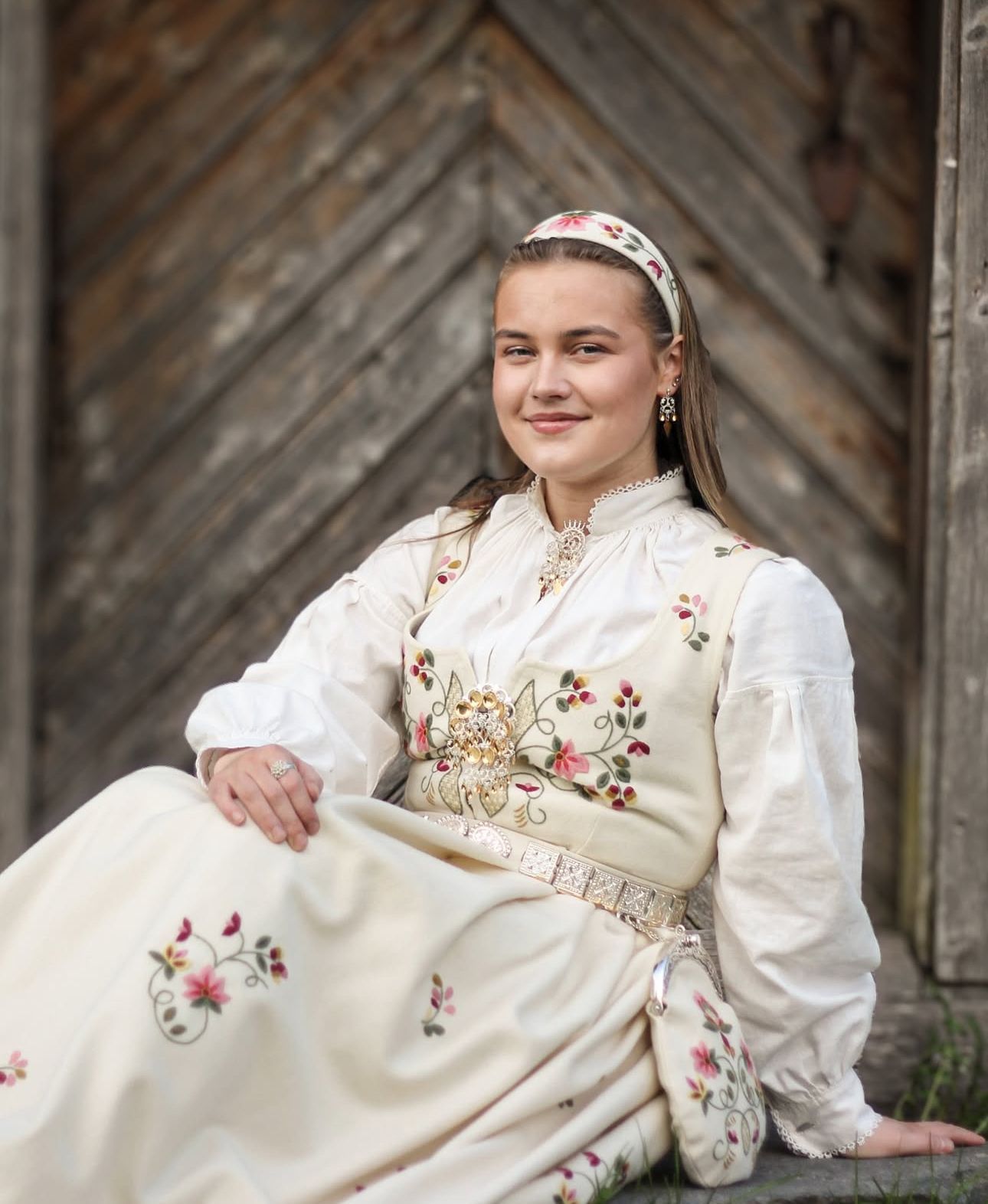 Traditional folk costume with floral embroidery and white dress against rustic wooden background.