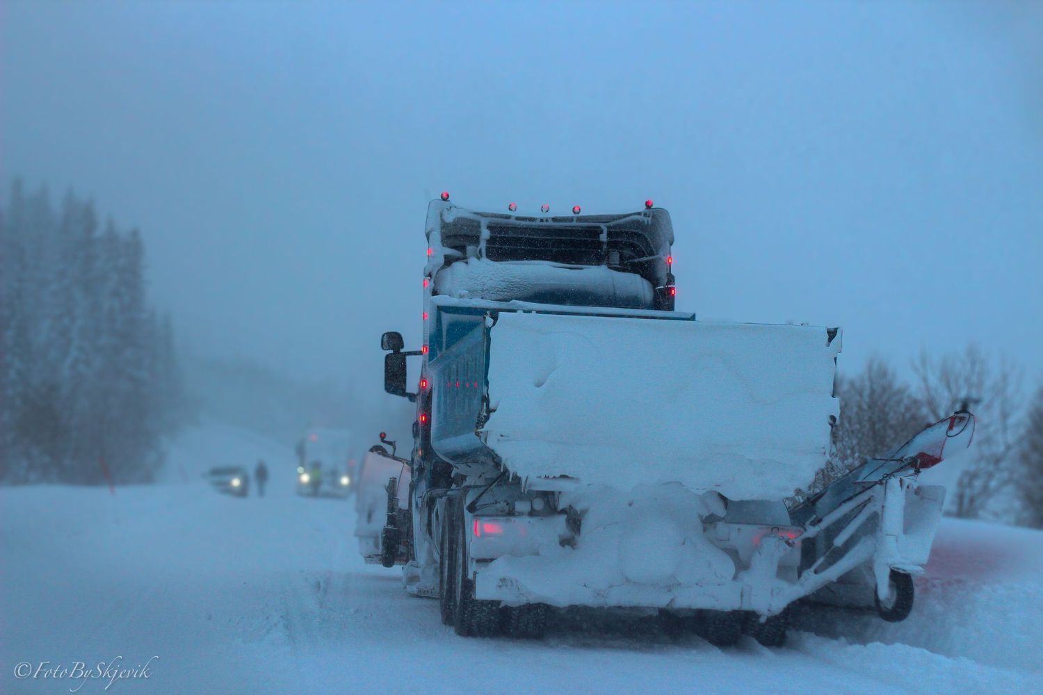 Snow-covered trucks and vehicles parked in foggy winter conditions.