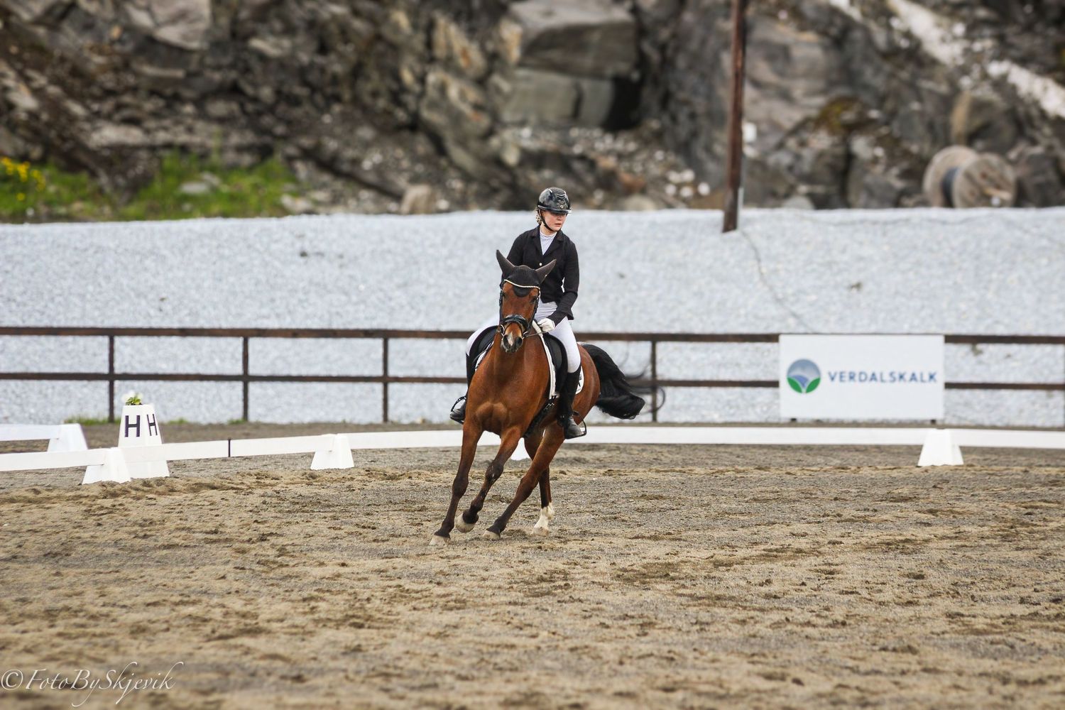 Equestrian rider on a bay horse performing dressage in an outdoor sand arena during a competition.