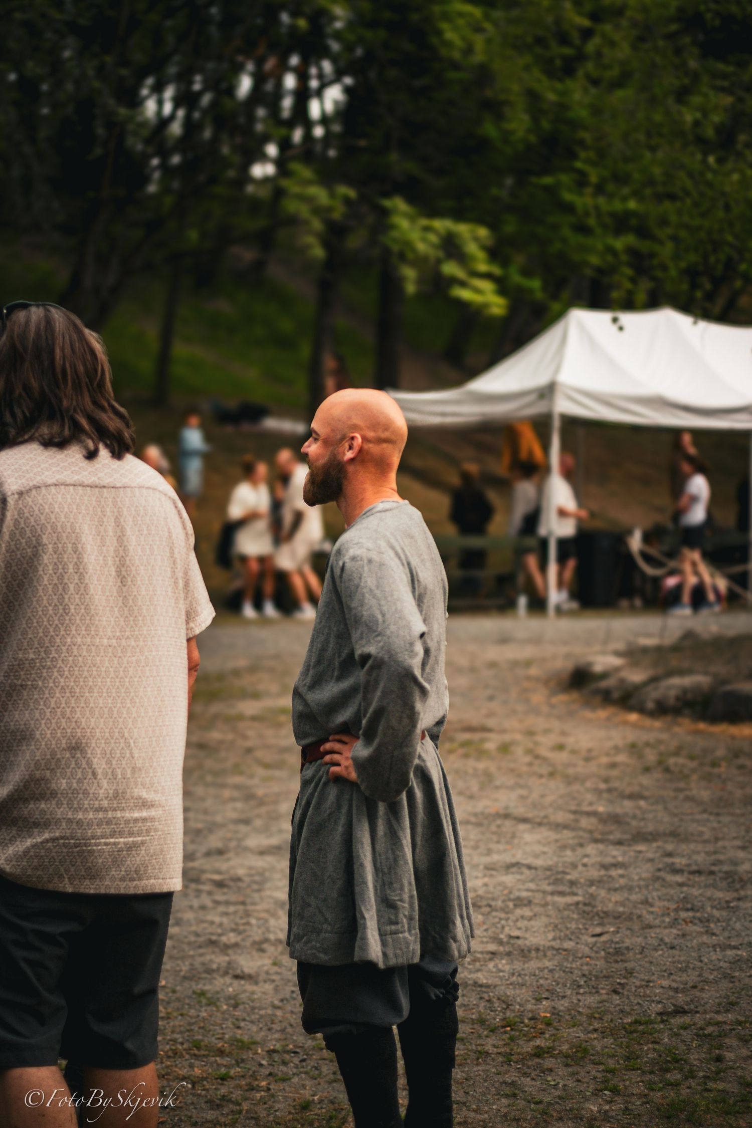 Two people stand together at an outdoor event with white tents visible in the background.