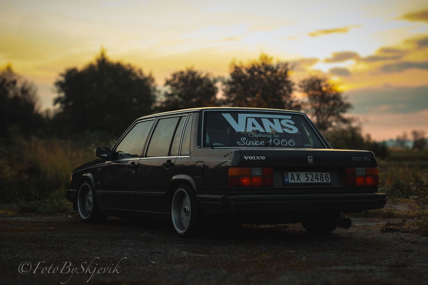 Vintage Volvo wagon silhouetted against a golden sunset sky with Vans sticker visible.