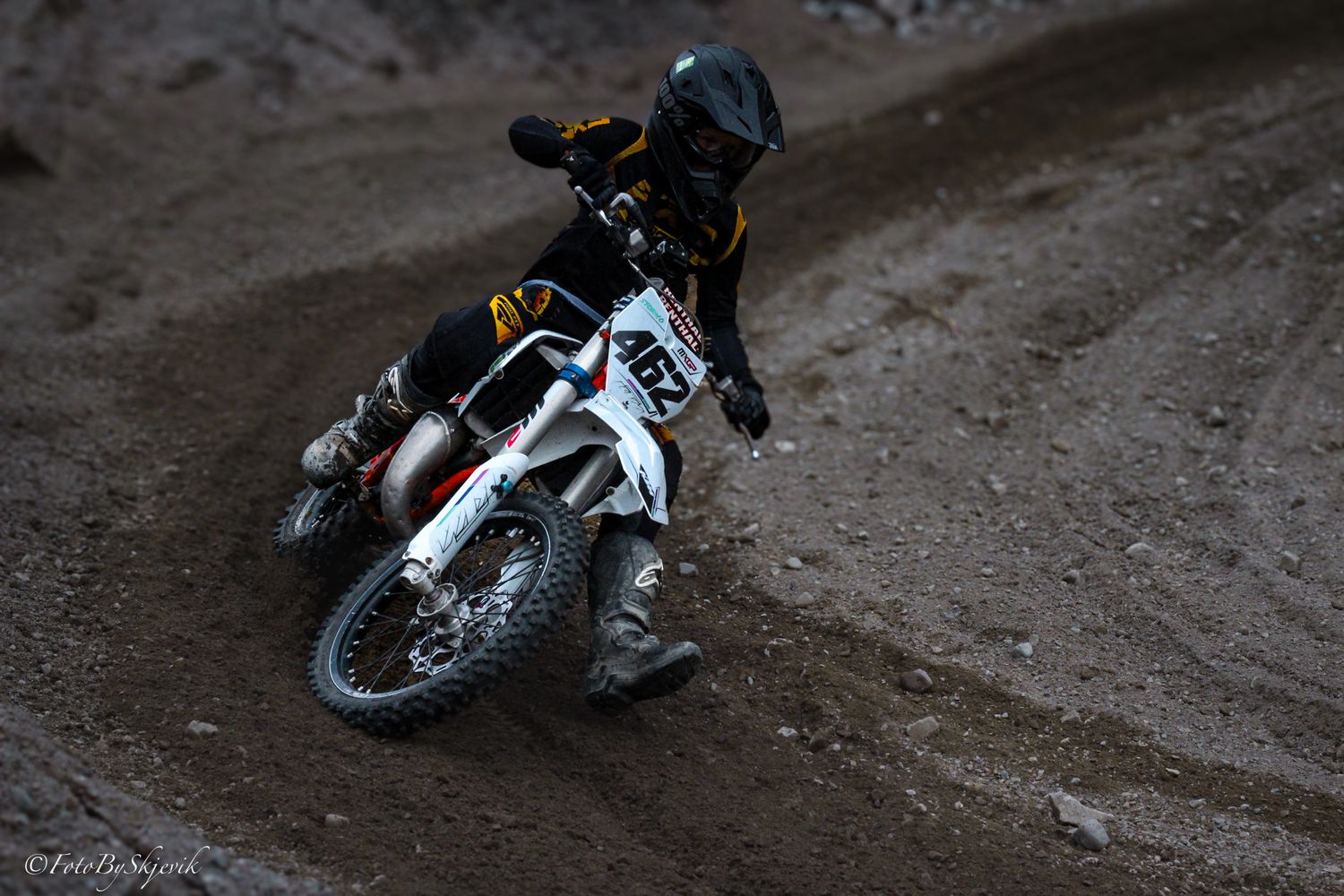 Dirt bike rider navigating a muddy turn on an off-road trail.