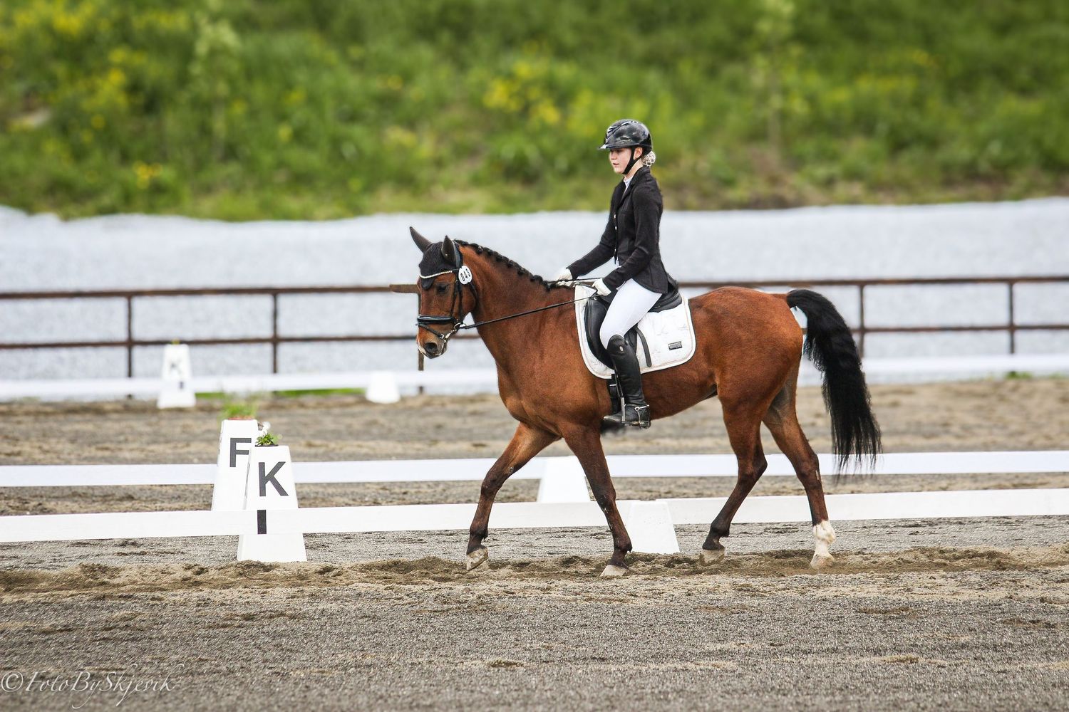 Bay horse and rider competing in dressage near letter markers FK in an outdoor riding arena.
