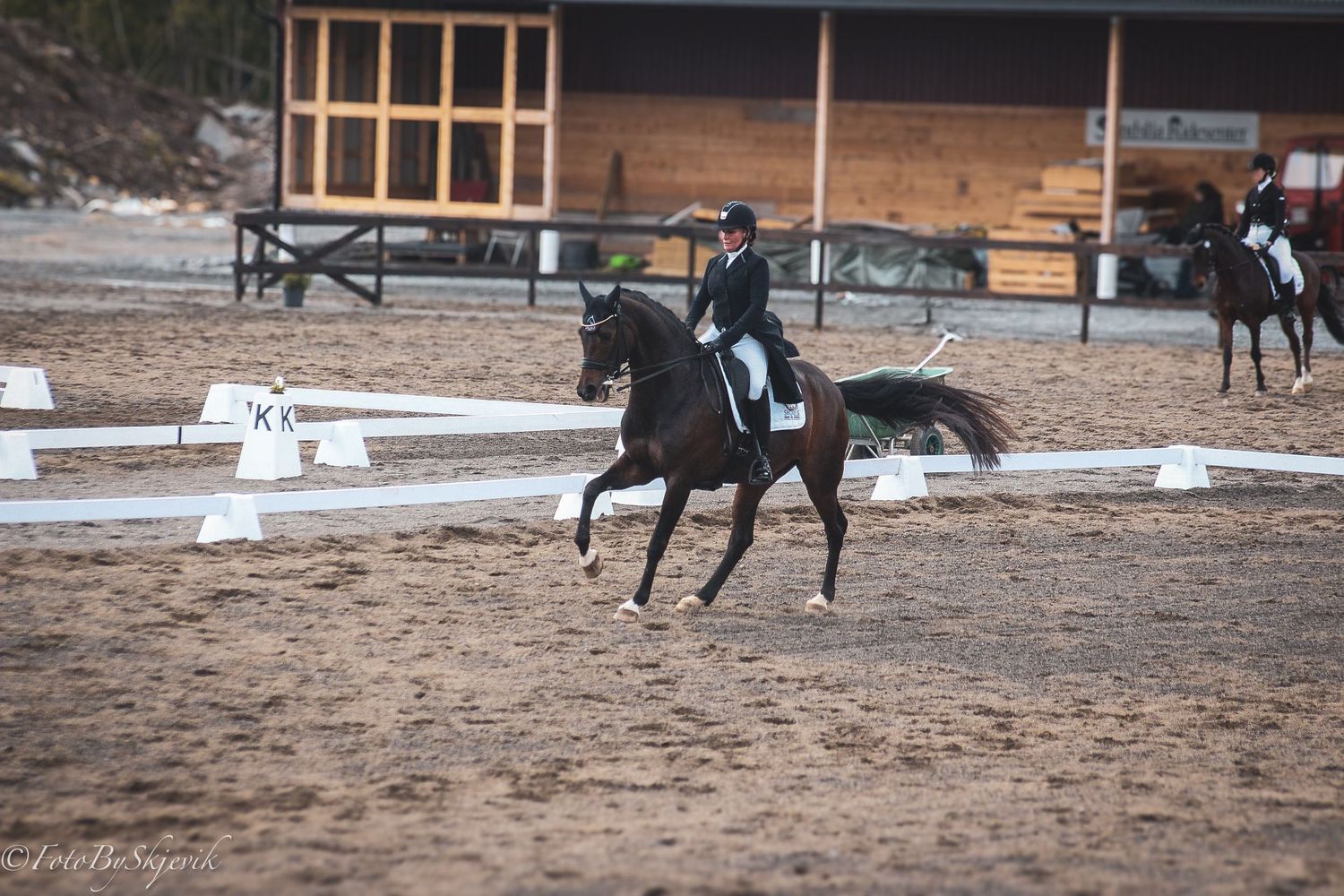 Equestrian in black riding a dark horse during a dressage competition in an outdoor arena.