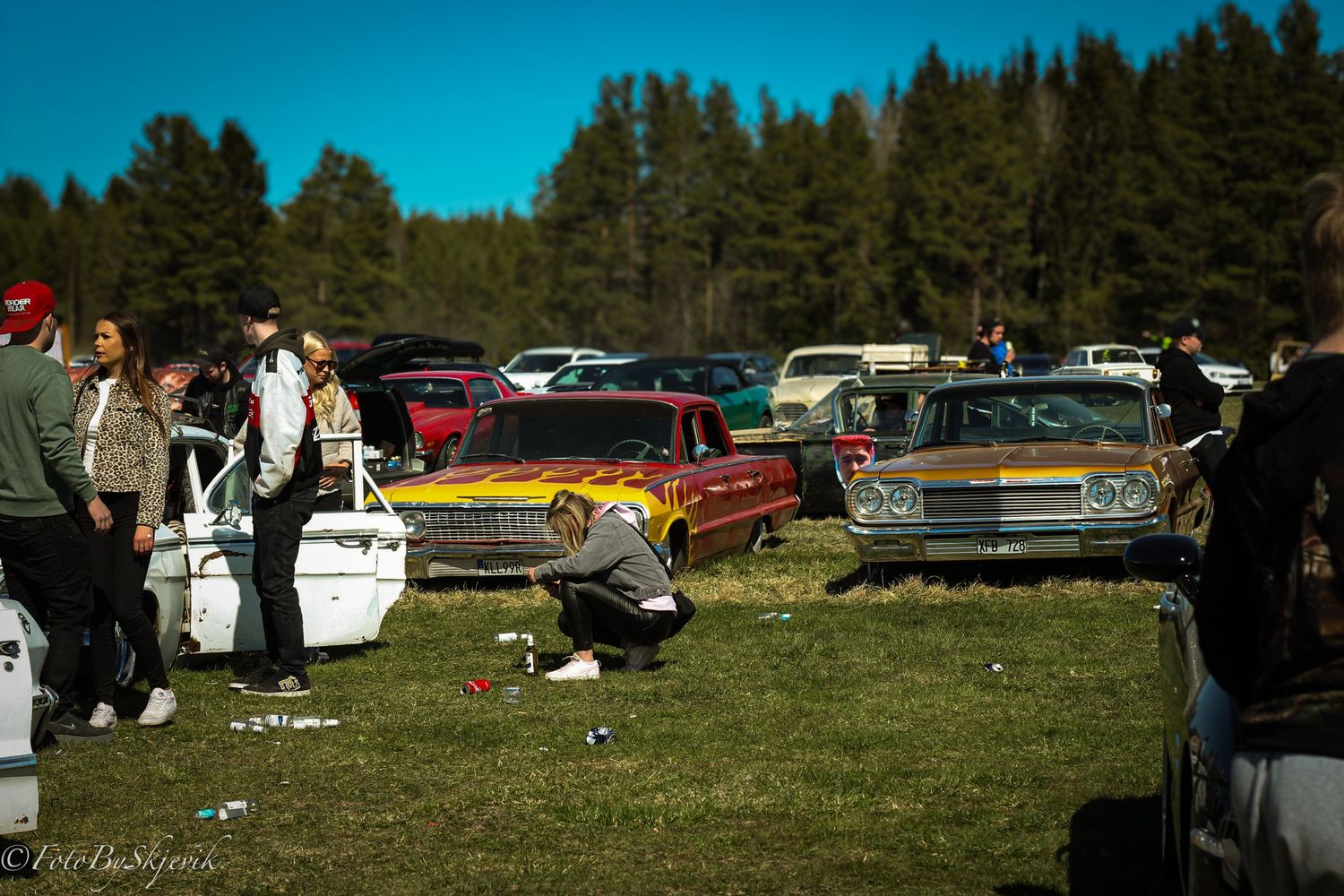 Wide angle shot of vintage automobiles displayed at an outdoor car show with trees in background.