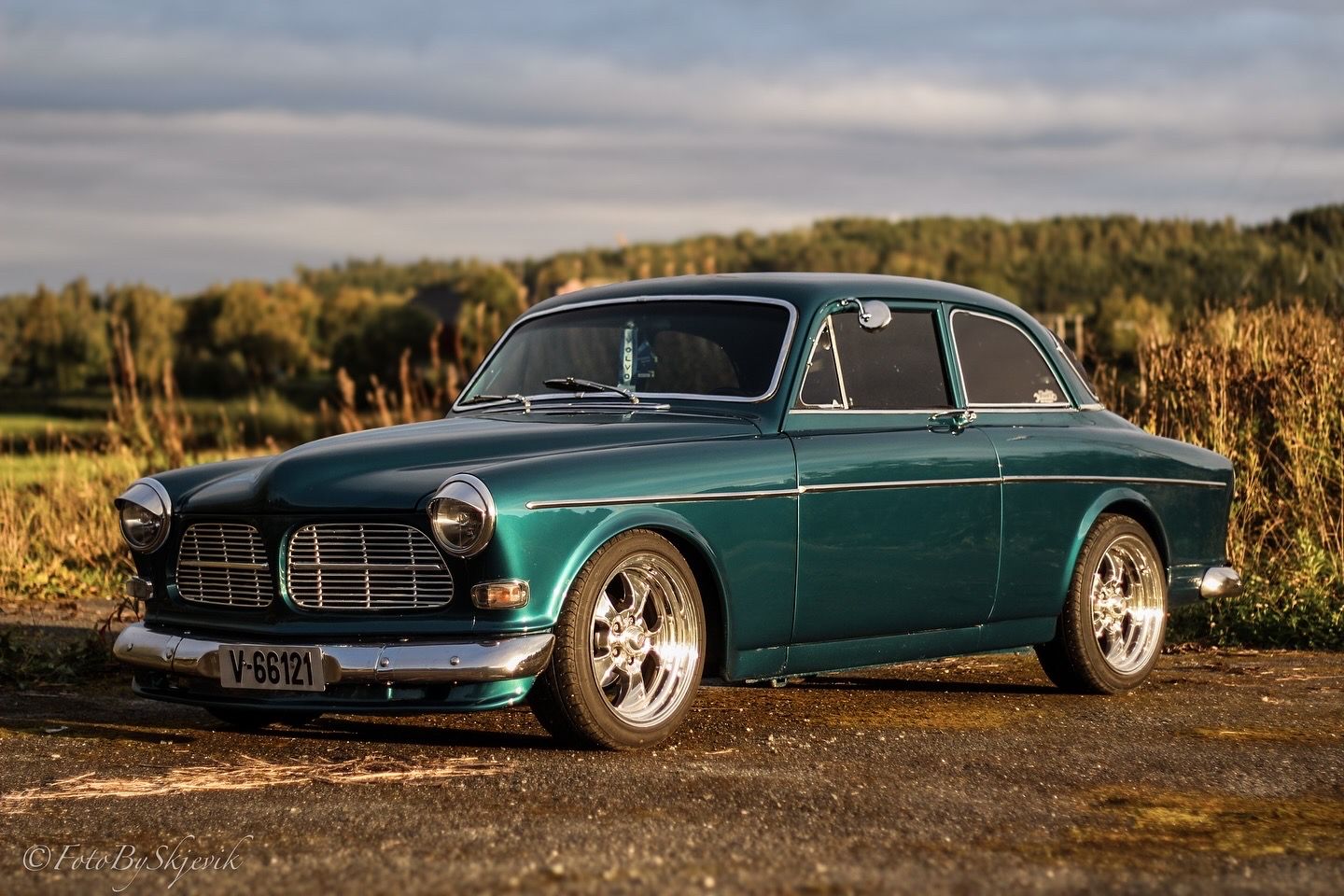 A vintage teal Volvo Amazon custom car photographed during golden hour with custom wheels.