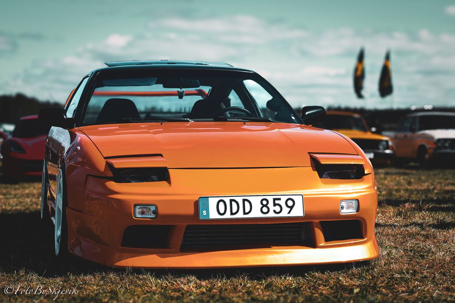Orange vintage sports car photographed at sunset with dramatic lighting.
