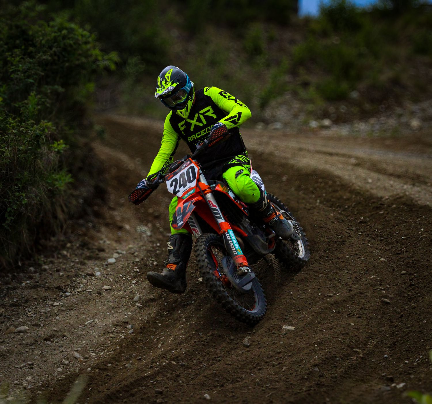 Dirt bike rider in neon gear navigating a muddy motocross track.