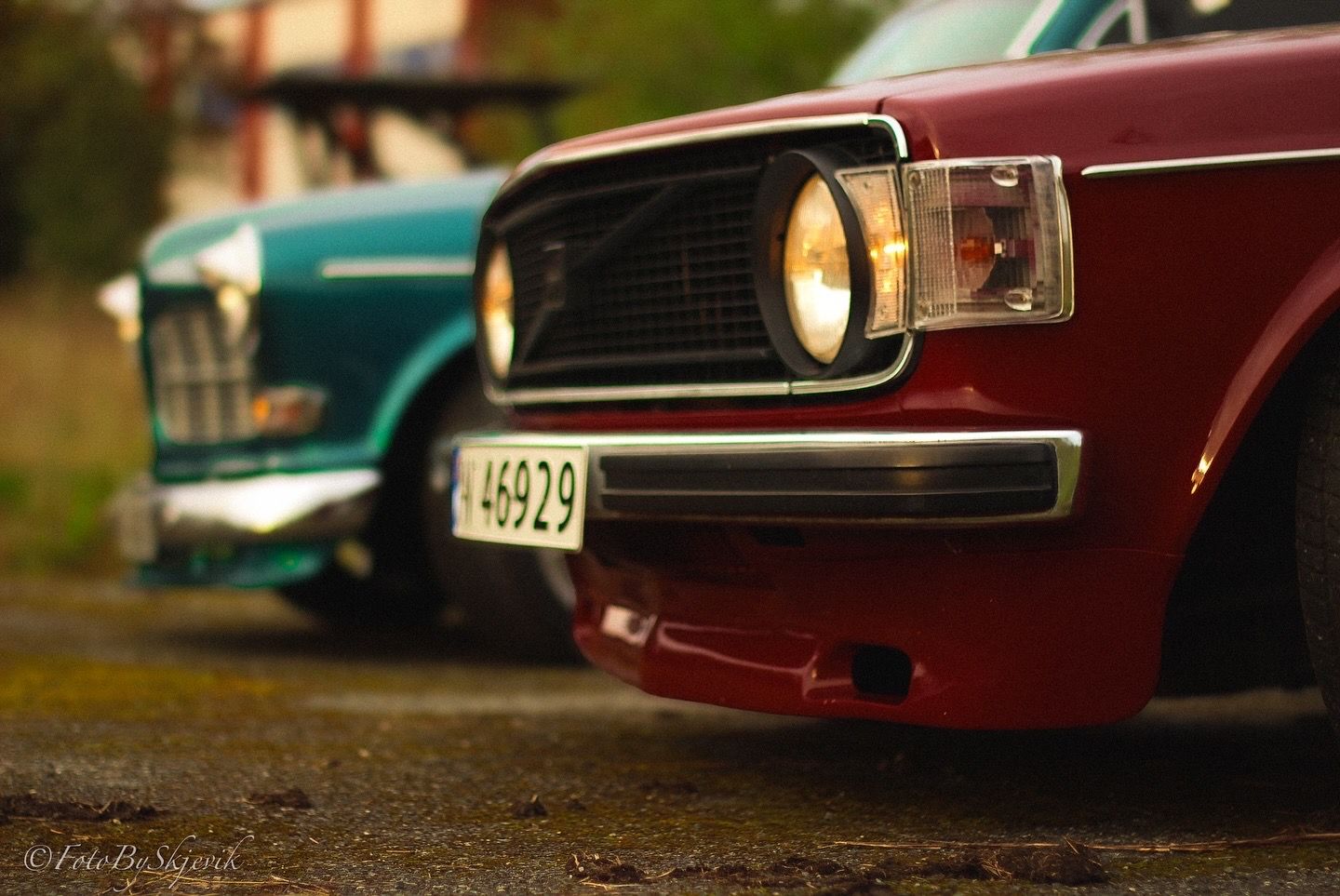 Close-up of vintage car headlights and grille in maroon color.