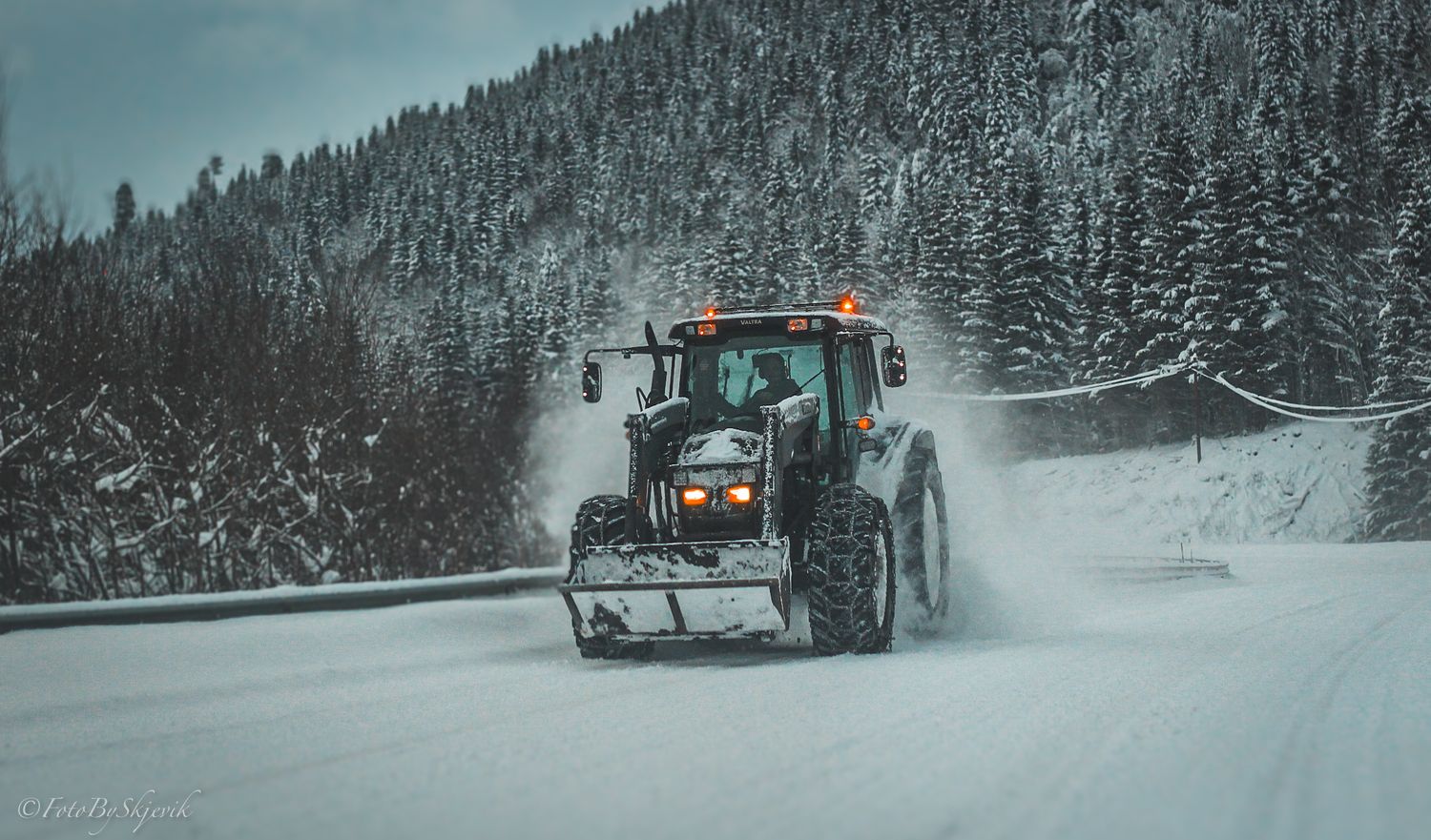 Snow removal vehicles working in tandem to clear snowy mountain roads surrounded by evergreen trees.