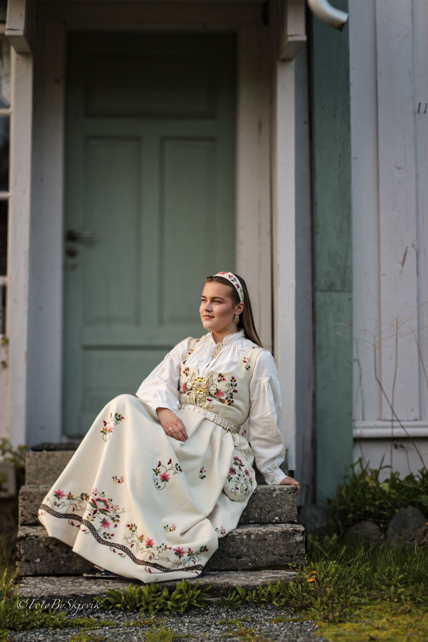 Traditional white embroidered dress with floral details photographed against a rustic building exterior.