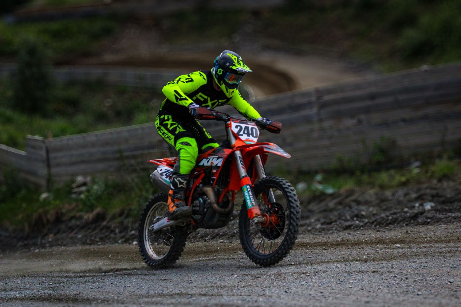 Motocross rider in bright green gear jumping over dirt track obstacles.