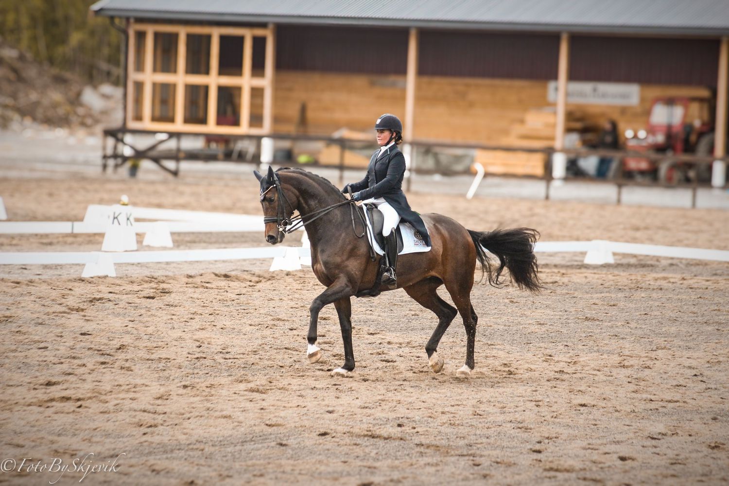 Horse riders performing dressage exercises in a sandy arena with wooden buildings.