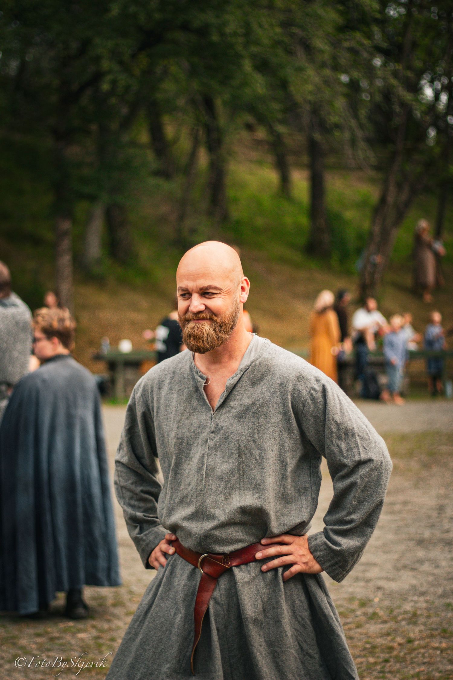Person wearing grey medieval tunic with leather belt at outdoor event.