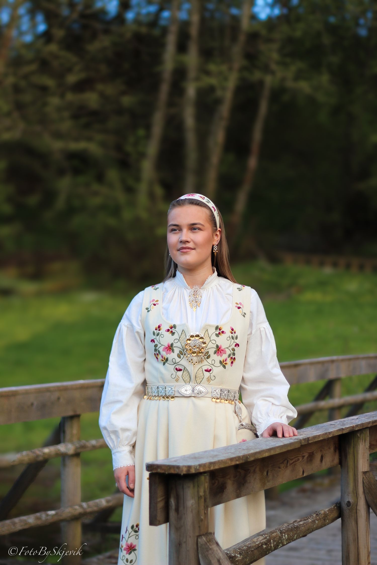 Traditional folk dress with floral embroidery photographed on wooden bridge.