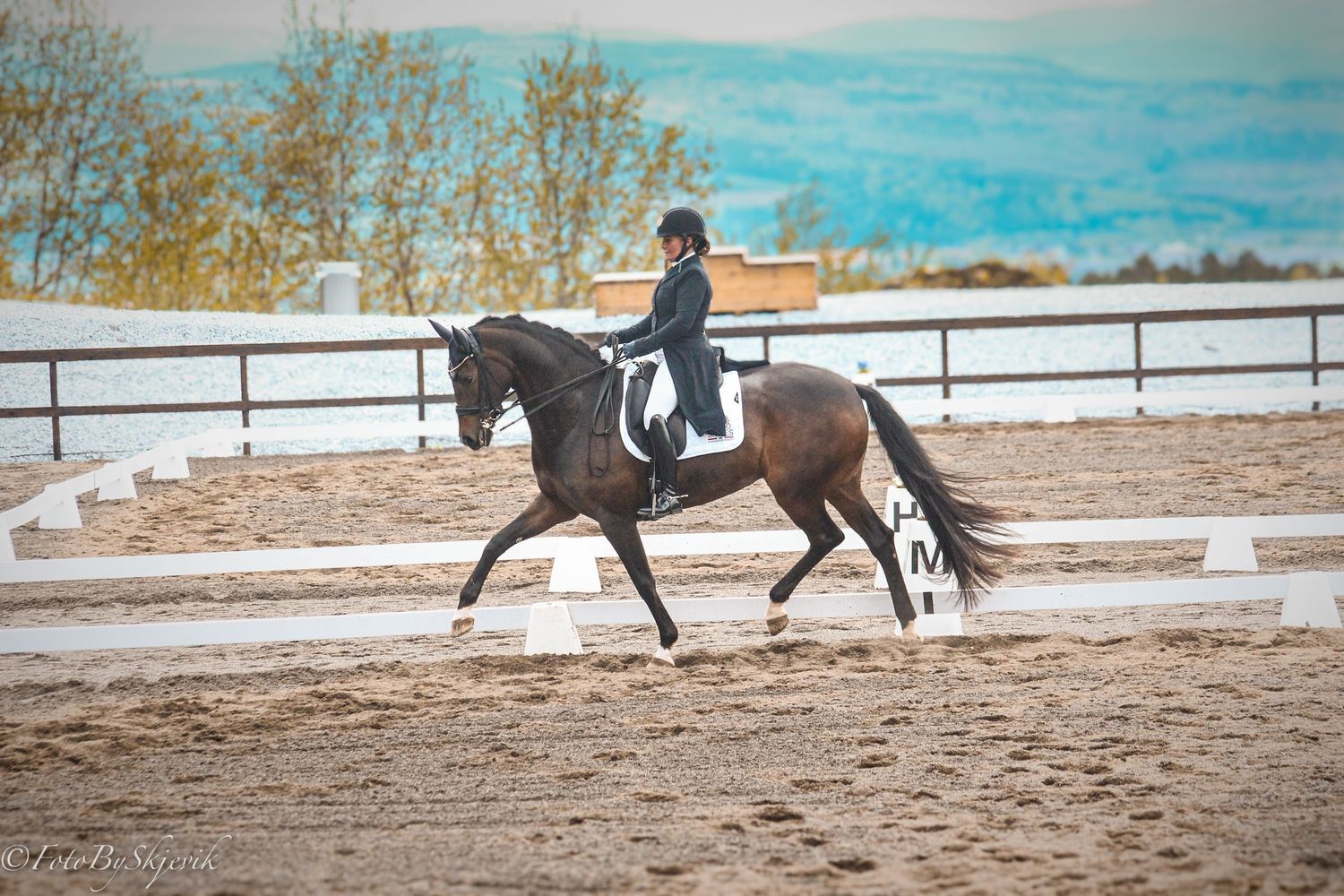 Equestrians practicing dressage in an outdoor arena with white fencing.