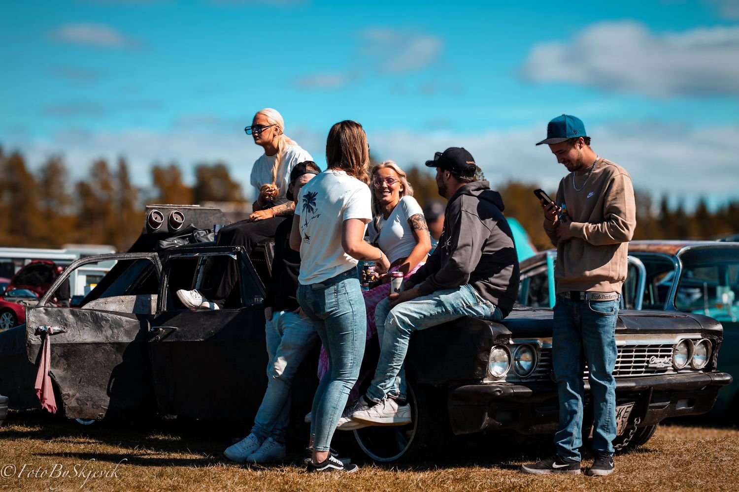 Group of people relaxing on cars at an outdoor gathering.