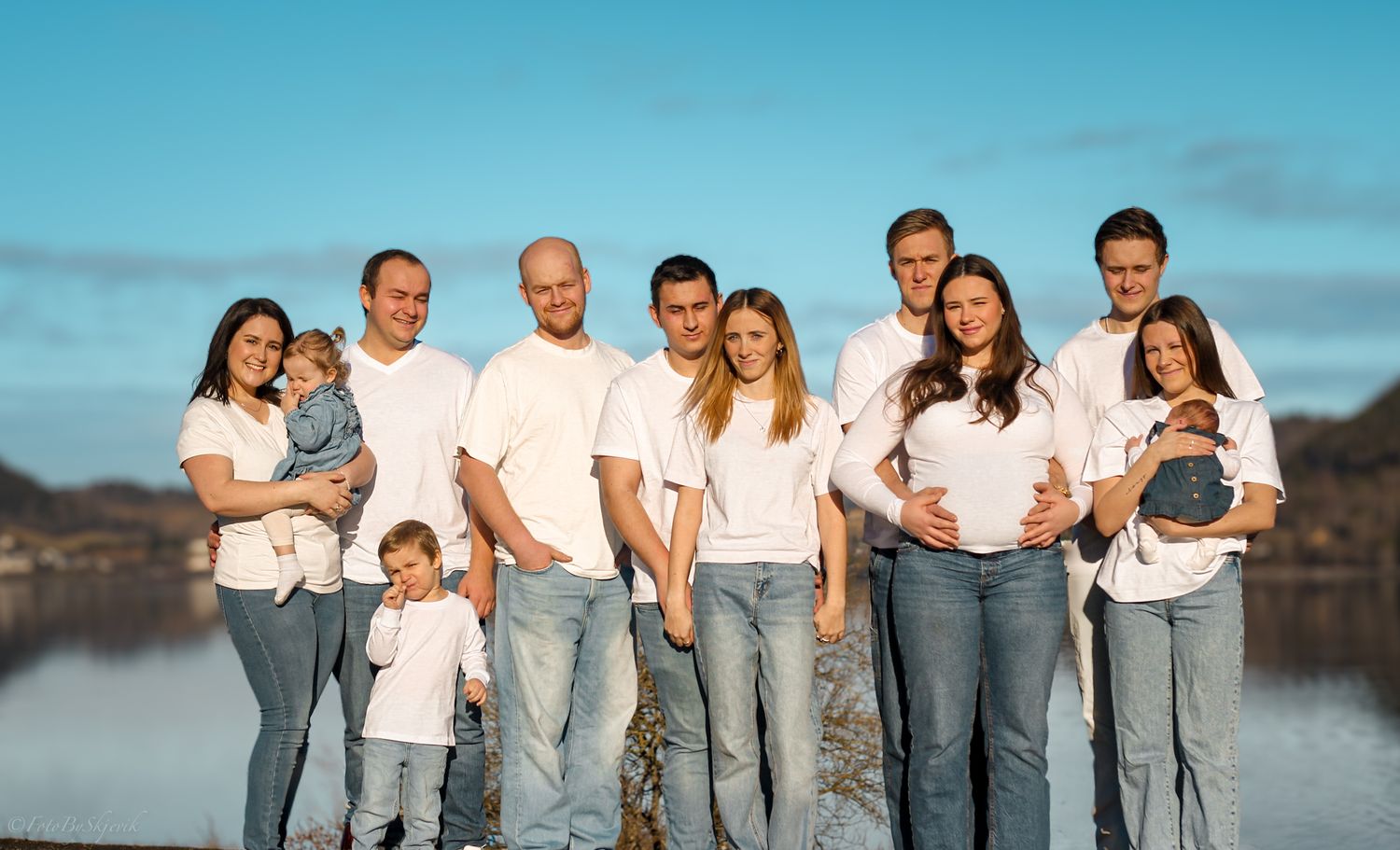 Group wearing coordinated white shirts and jeans posing together outdoors against blue sky.