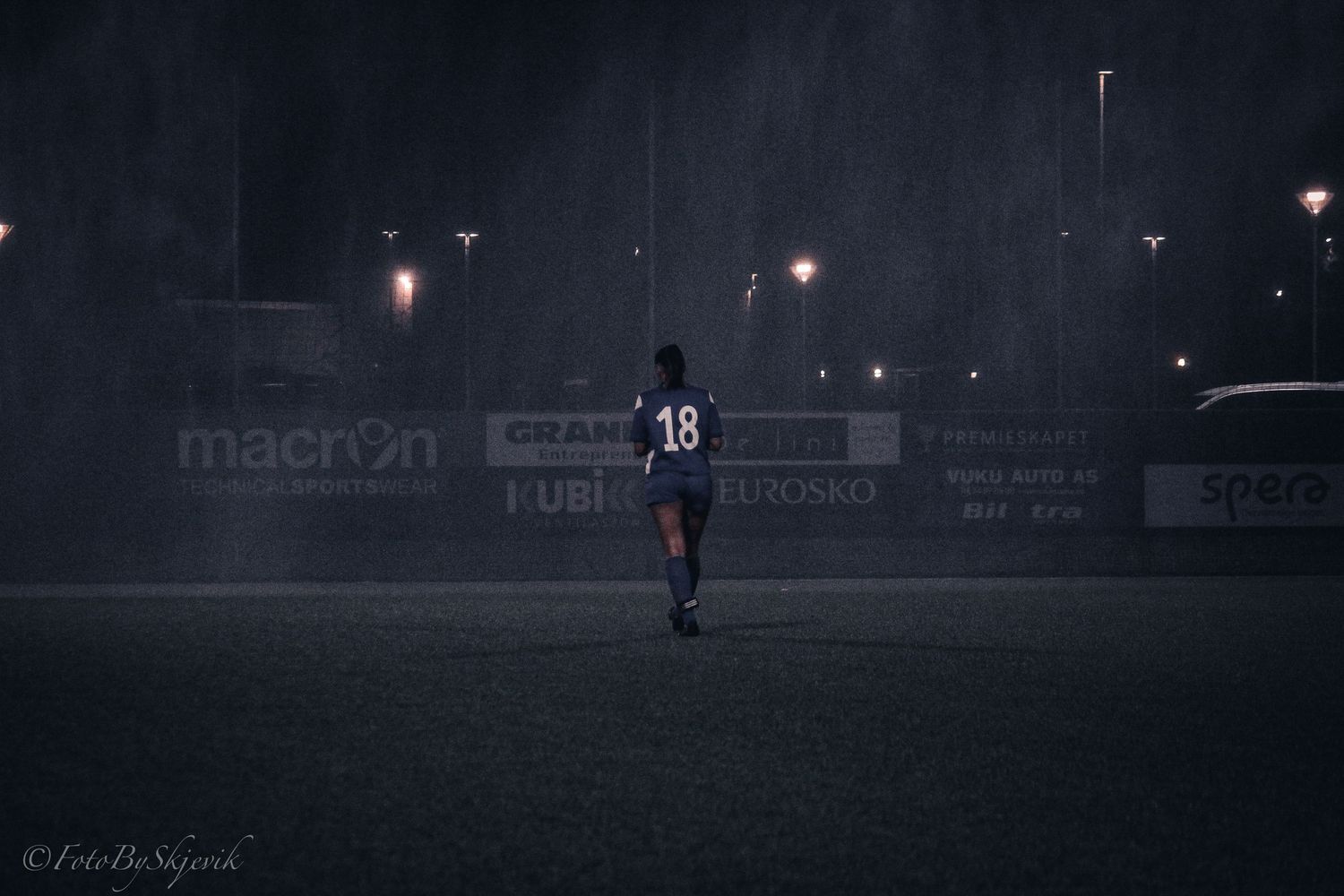 Soccer player on dark field illuminated by stadium lights at night.