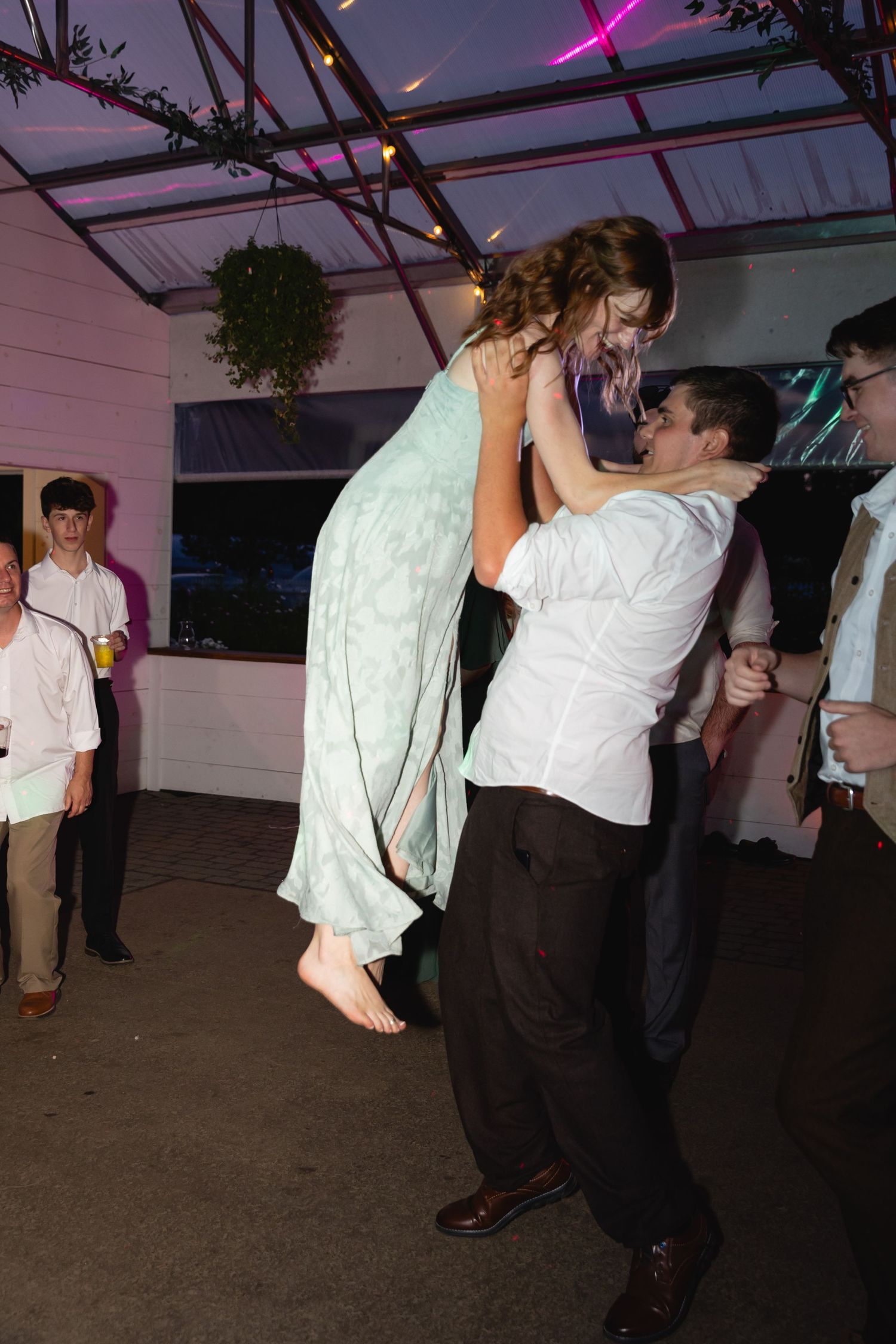 People dancing together at a party with pink lighting and white decor visible in the background.
