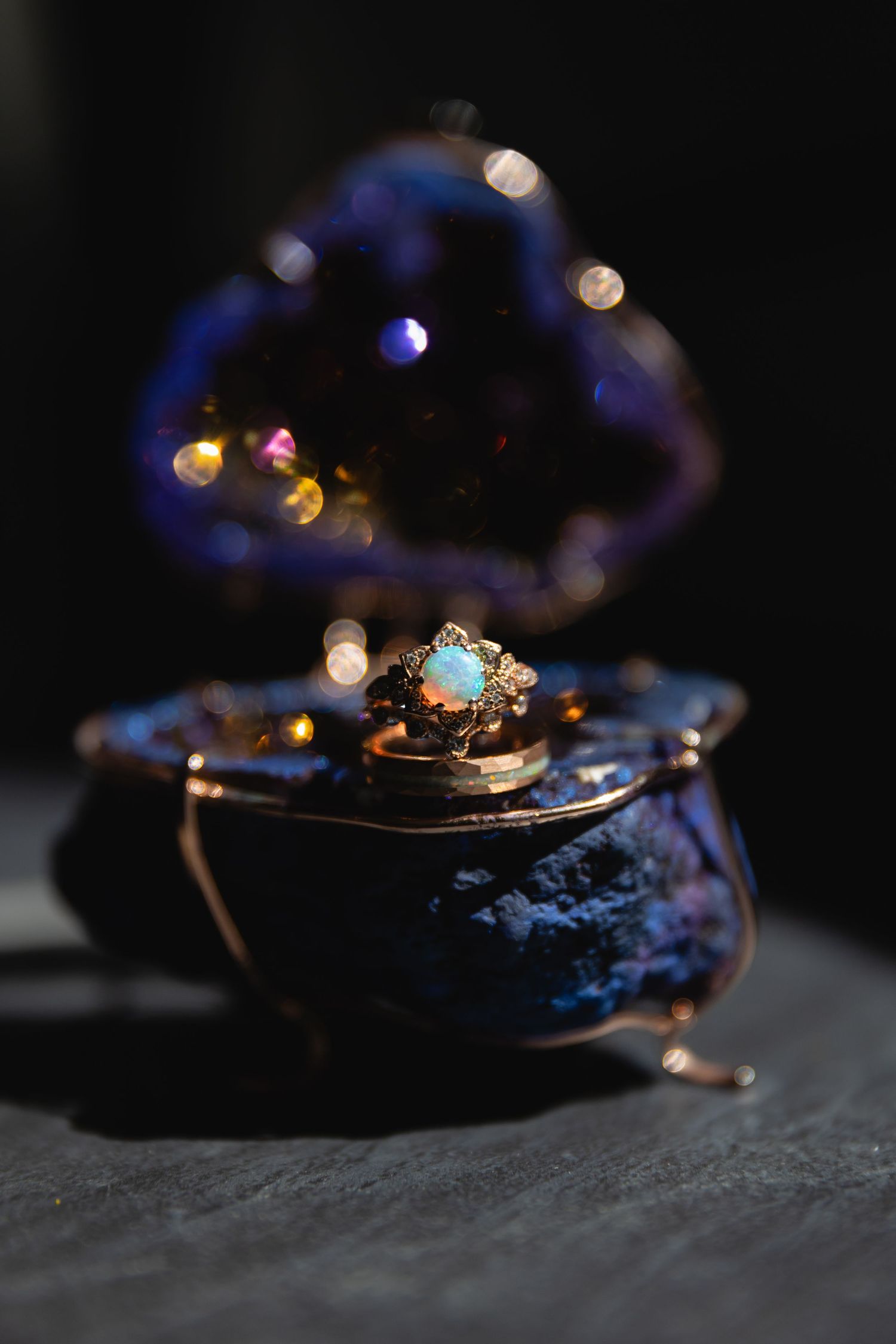 A vintage blue ring box with a delicate opal and gold ring displayed against a dark background with bokeh lights.