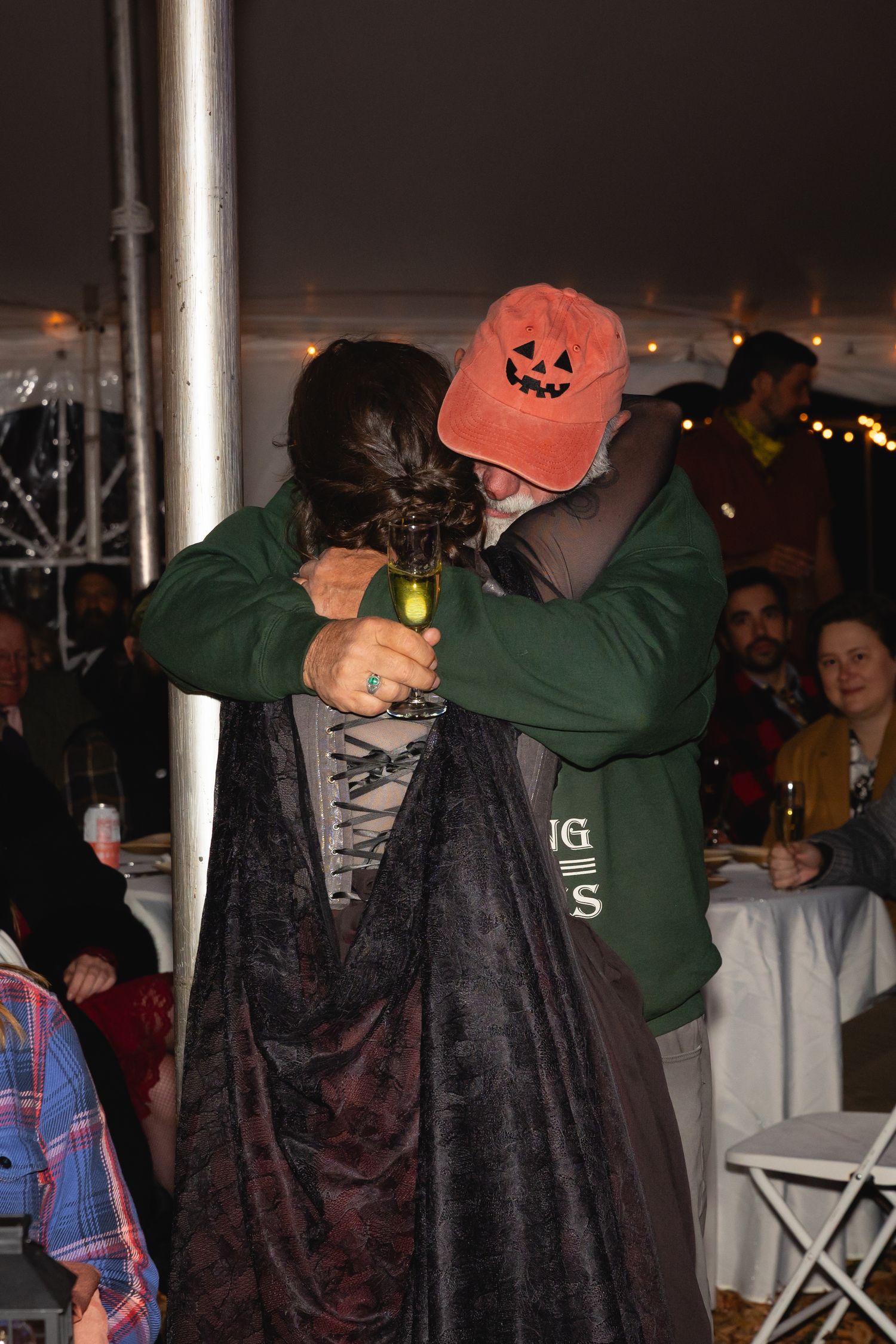 People dancing and celebrating at a Halloween party with someone wearing a dark cape and orange baseball cap.