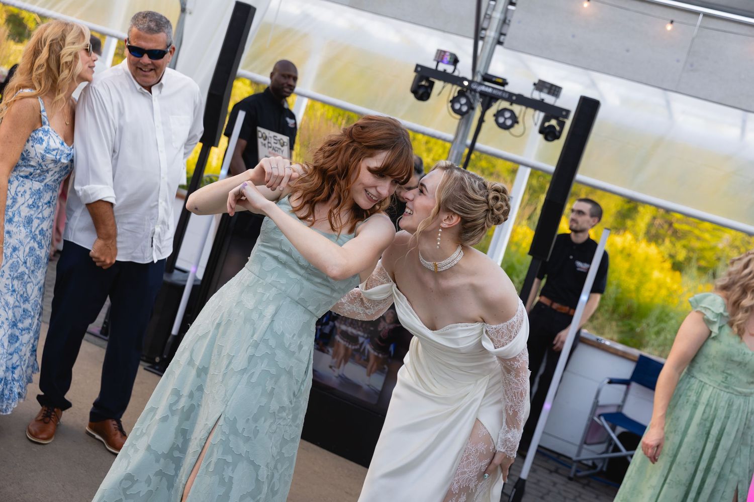 Two people in formal dresses dance together at a celebration while others watch in a room decorated with yellow accents.