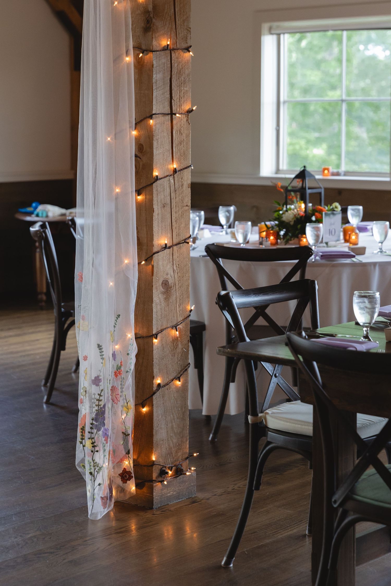 Wedding reception venue decorated with string lights wrapped around wooden beams and elegant table settings.