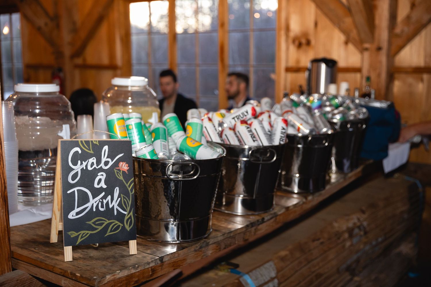 Several dark beers lined up on a rustic wooden bar counter with a chalkboard sign in a barn-style venue at dusk.