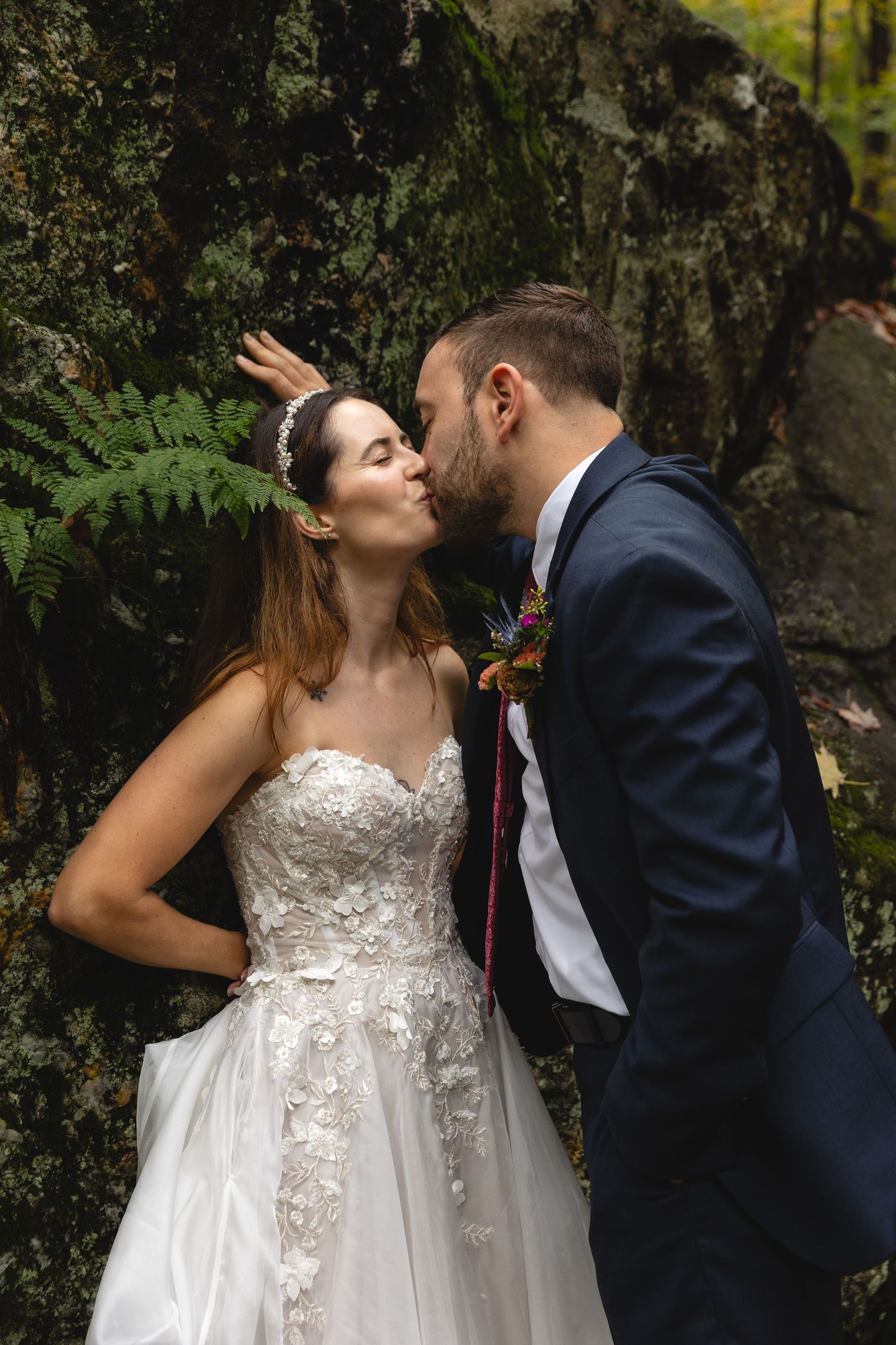 A tender romantic moment captured against a mossy rock wall in a forest setting.