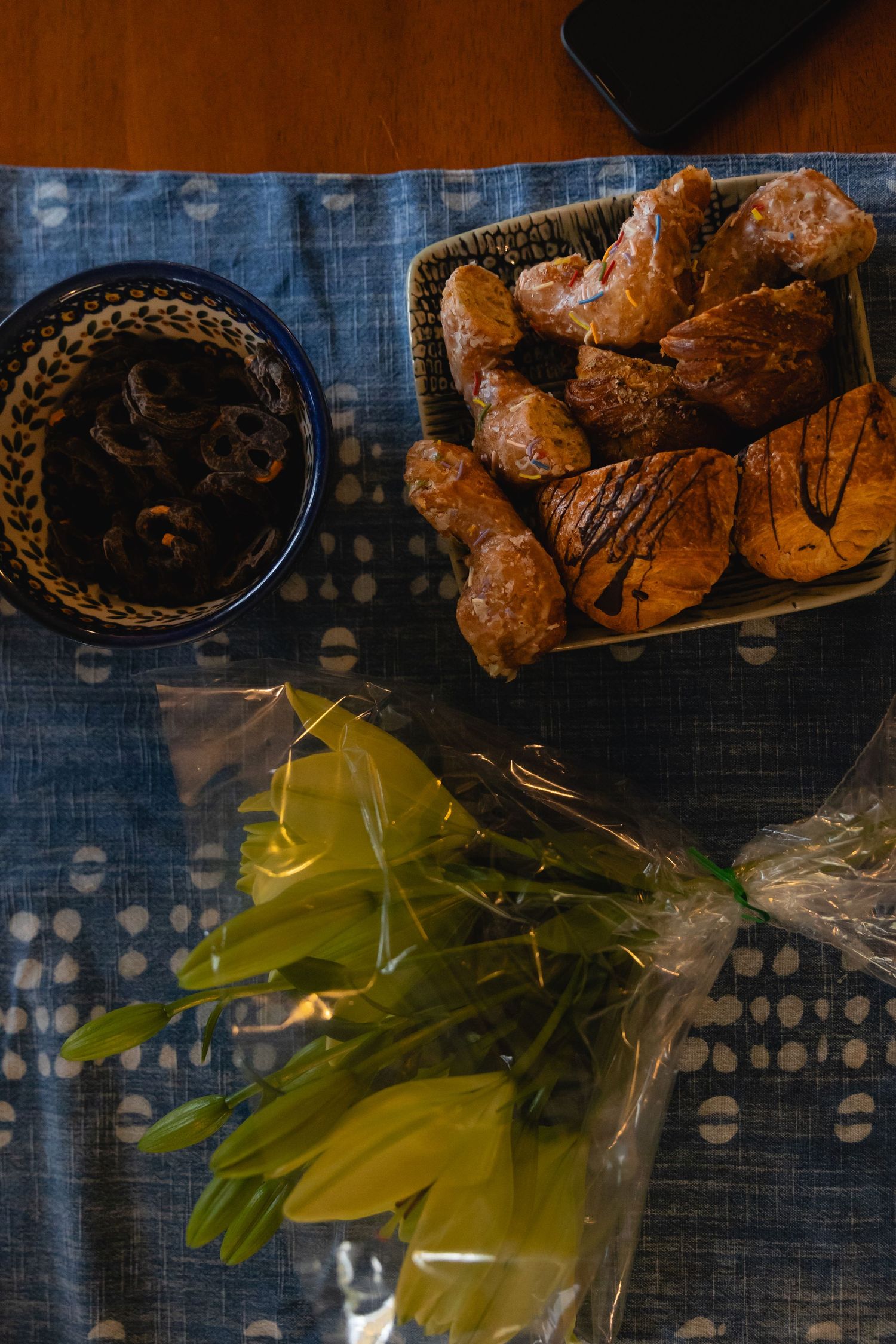 Overhead view of chocolate-drizzled pastries in a basket with yellow flowers and dark sauce on blue patterned cloth.