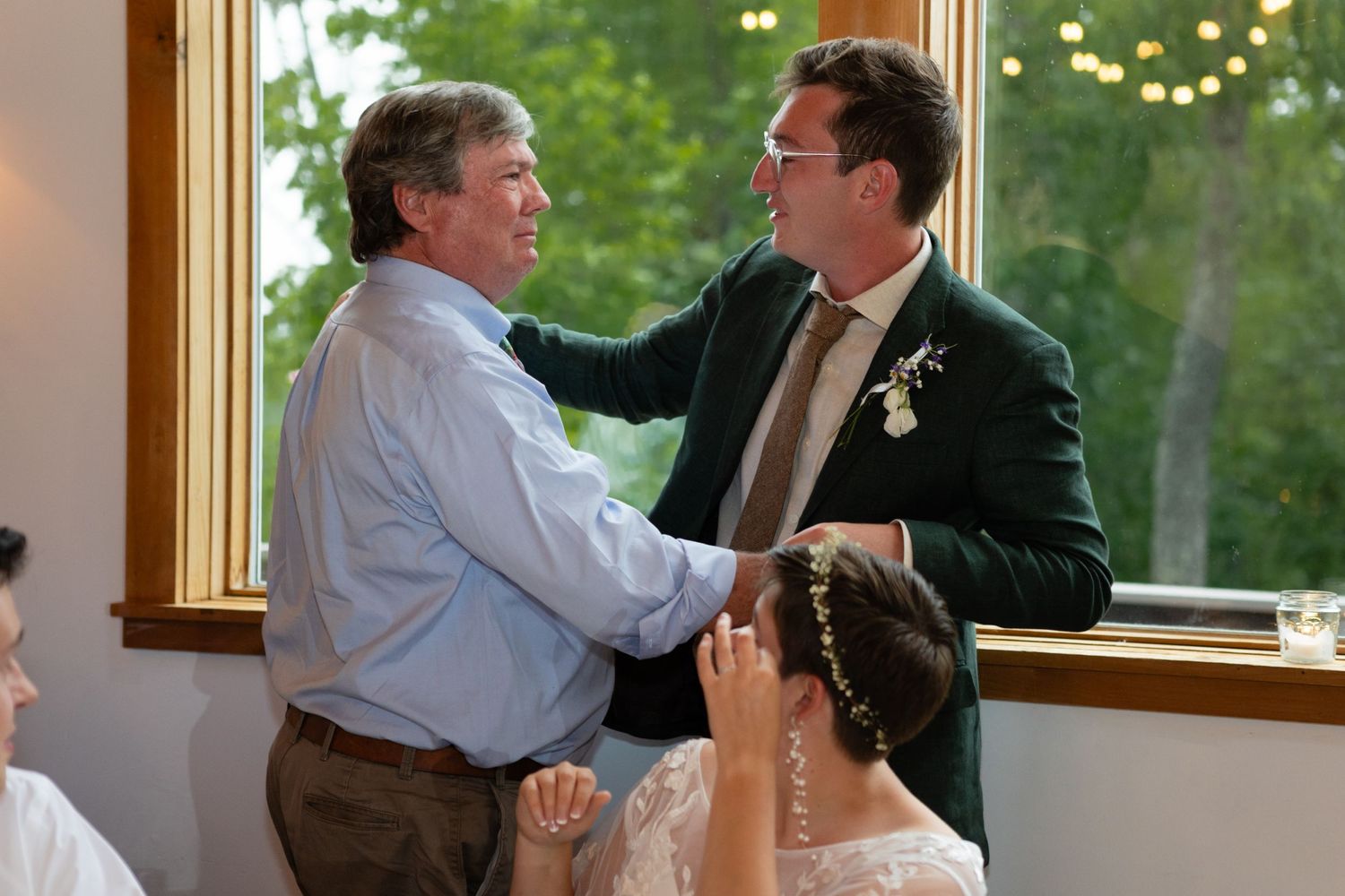 Emotional moment during wedding speeches by large windows in rustic venue.