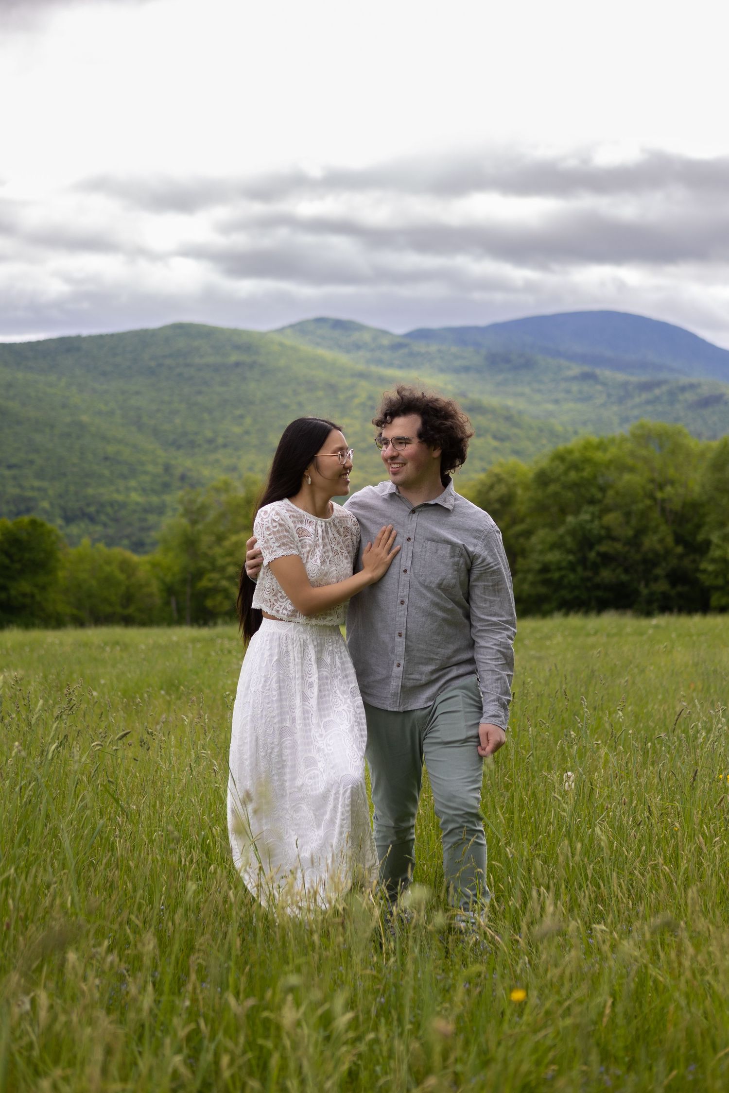 A couple shares a tender moment in a meadow with misty mountains in the background.