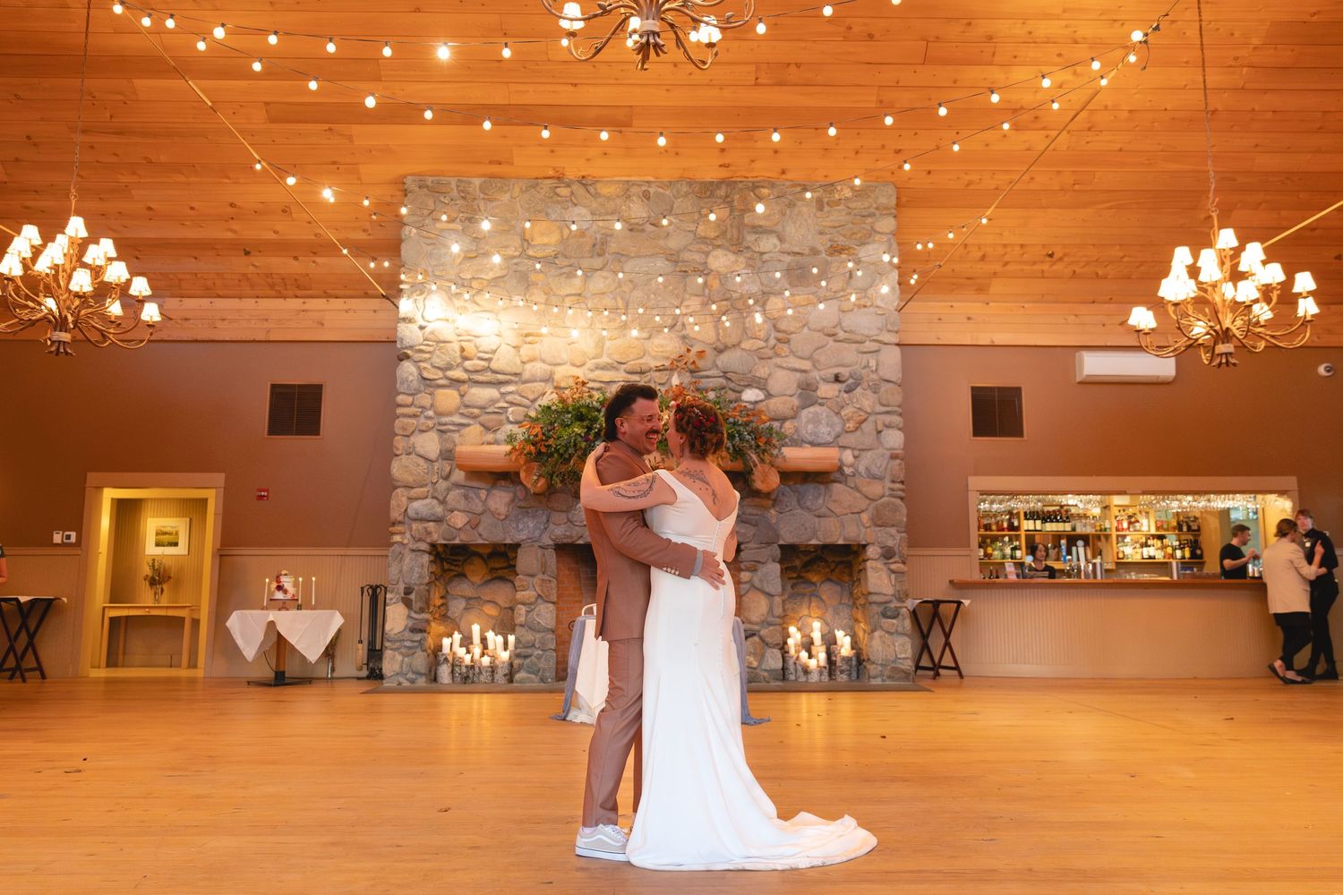 A couple dances in an elegant rustic venue with string lights and stone fireplace.