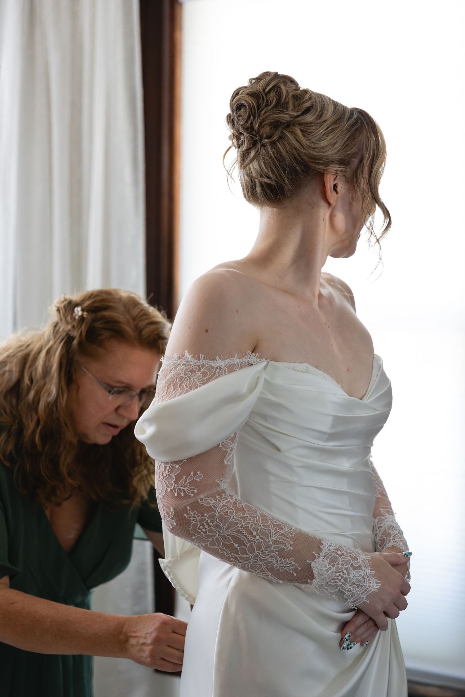 A sequence showing the final adjustments and fitting of a white lace wedding dress in a sunlit room.