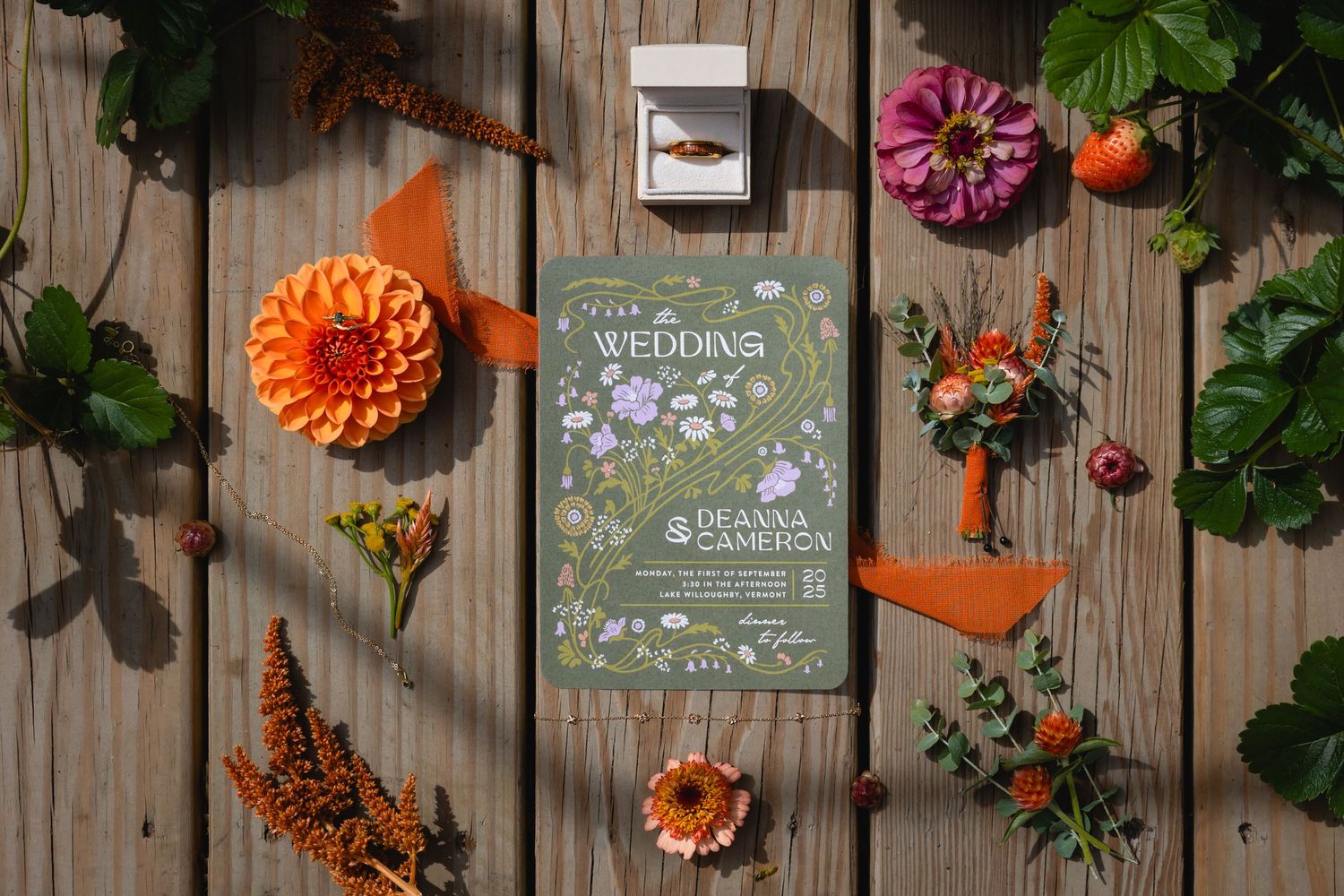 A garden-themed book lies on wooden planks surrounded by orange dahlias, pink flowers, and green foliage.