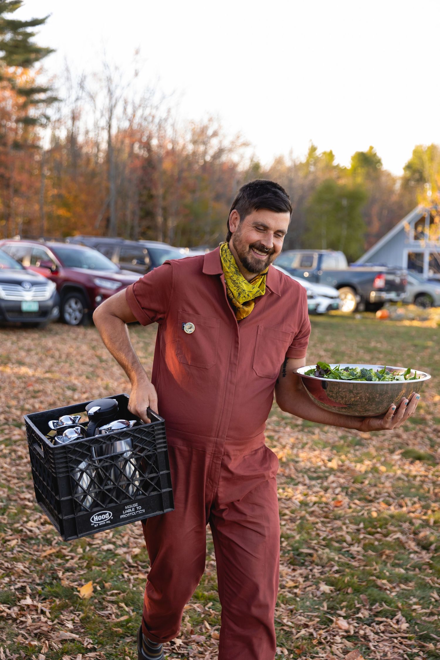 Person in burgundy jumpsuit collects fresh produce and groceries from delivery crates in autumn setting.