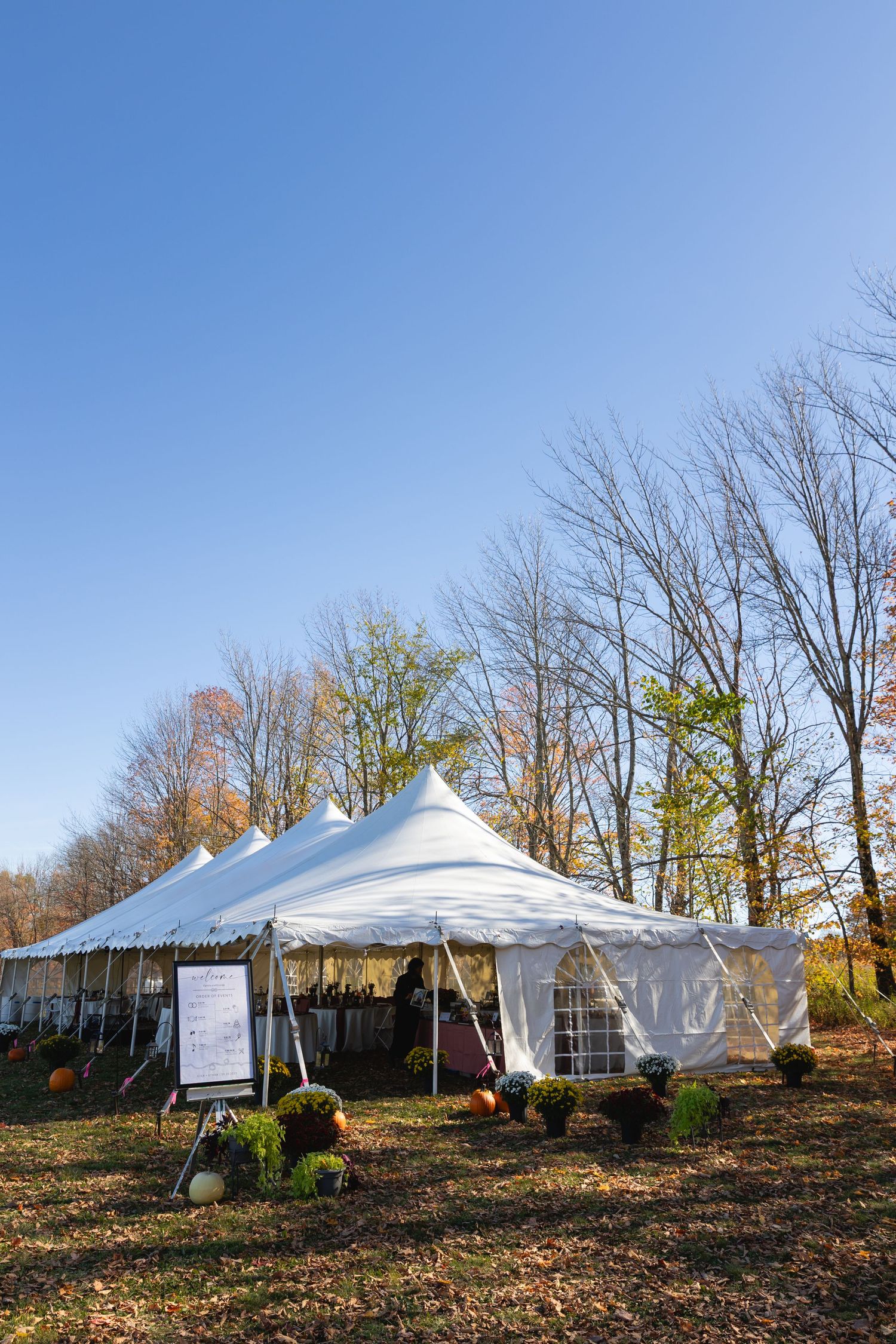 White event tents set up on a hillside with autumn trees and fallen leaves in the background under blue skies.