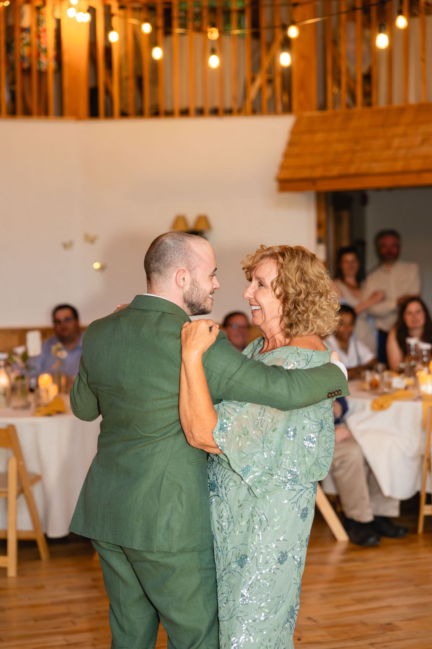 Couple in green attire dances together during wedding reception in rustic venue with wooden floors.