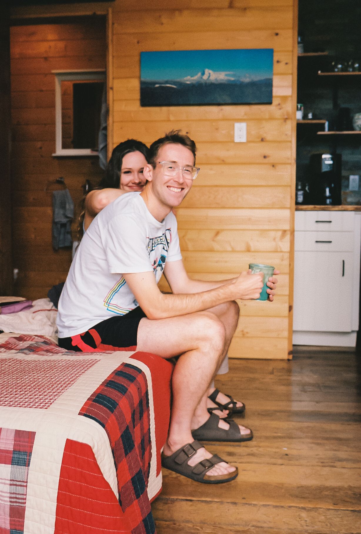 Two people relaxing in a cozy cabin interior with wood paneling and a mountain landscape painting on the wall.