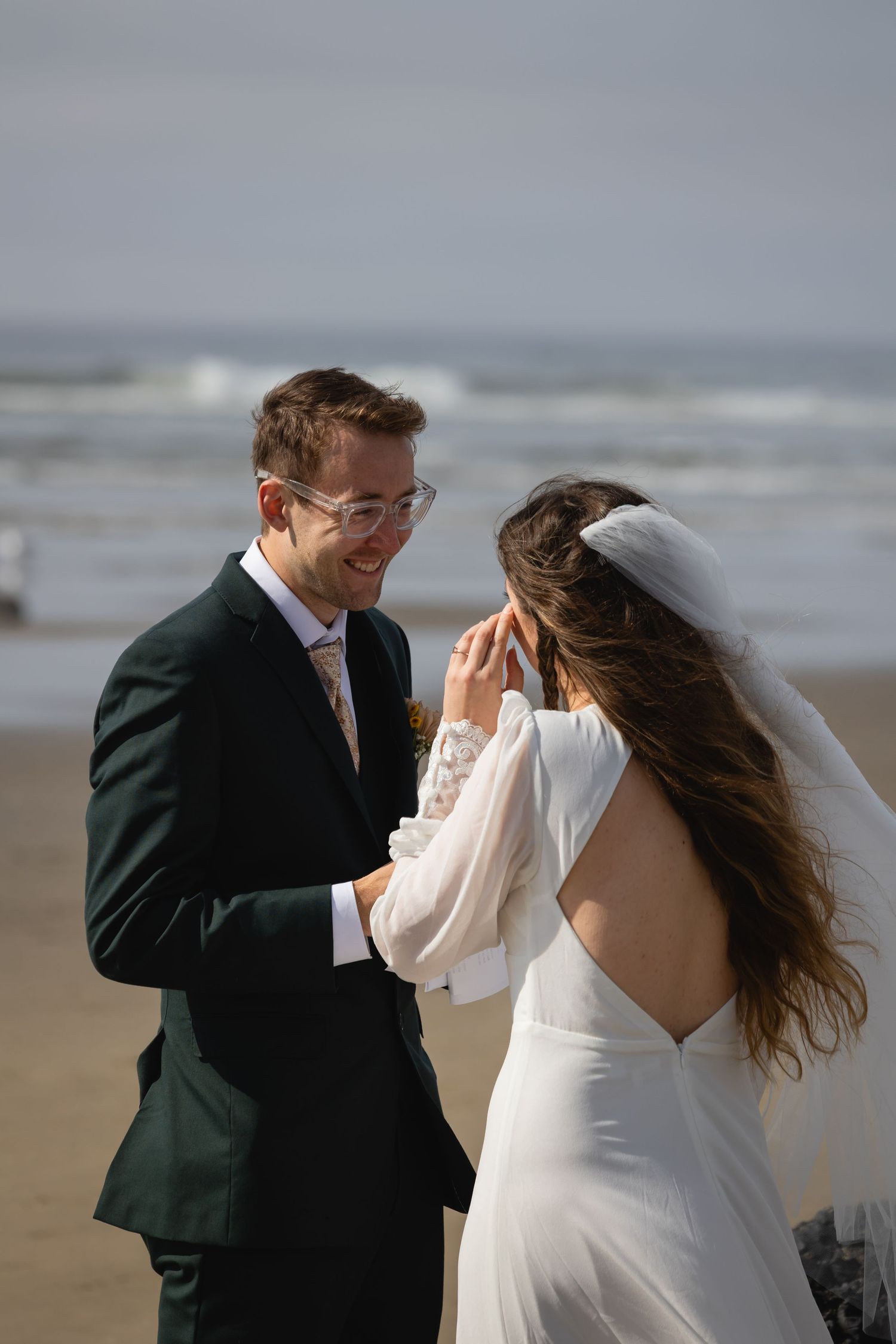 A couple shares a joyful moment together on a windy beach during their wedding celebration.